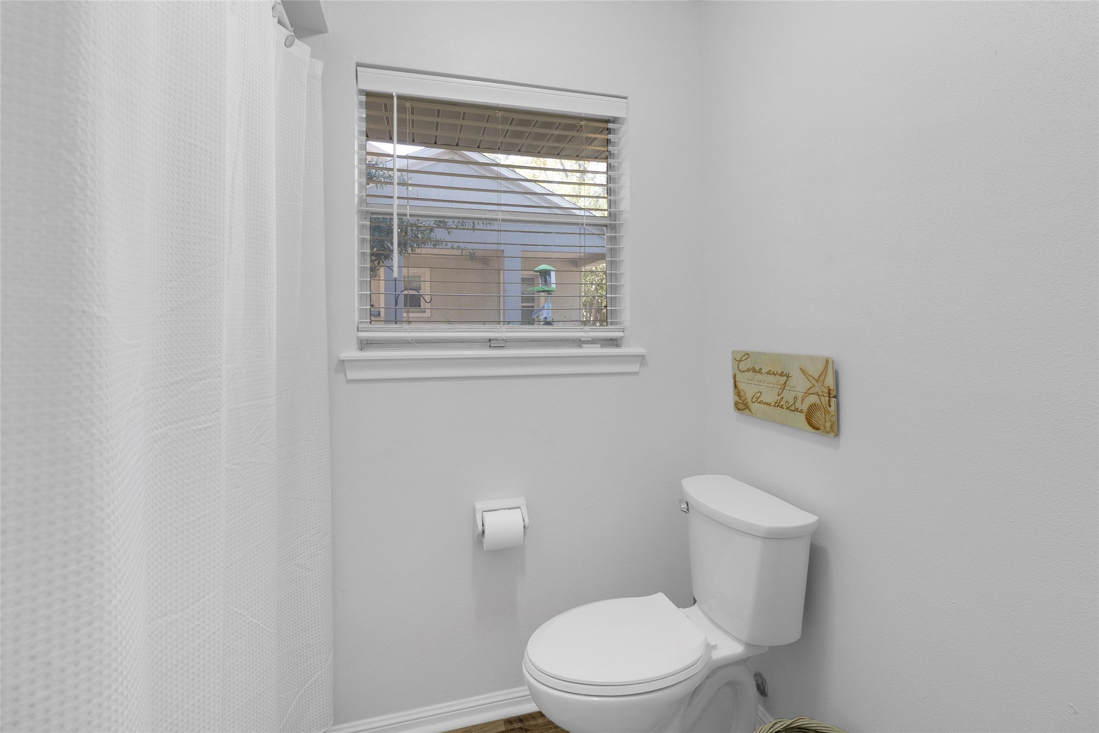 Bright and cozy bathroom featuring a window for natural light, a modern toilet, and a shower with a clean, white curtain.