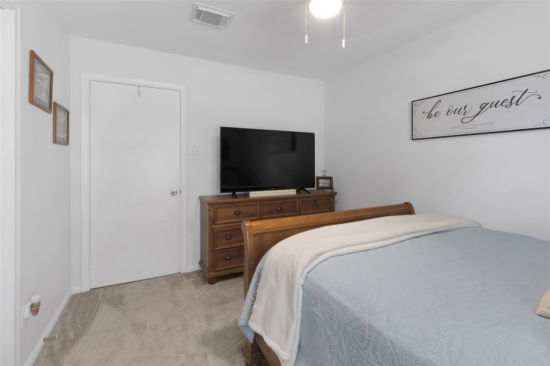 Generous bedroom with a plush carpet, stylish wooden furniture, and a welcoming wall sign, perfect for relaxation.