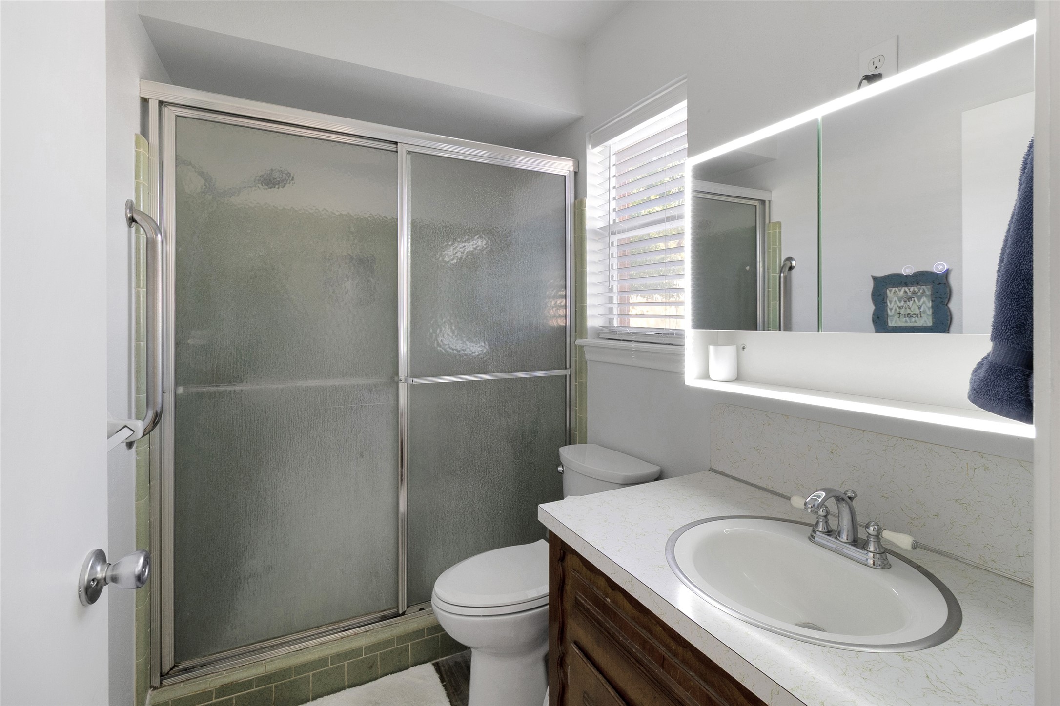 Bright bathroom featuring a shower with sliding glass doors, sleek vanity, and an illuminated mirror, creating a clean and inviting space.