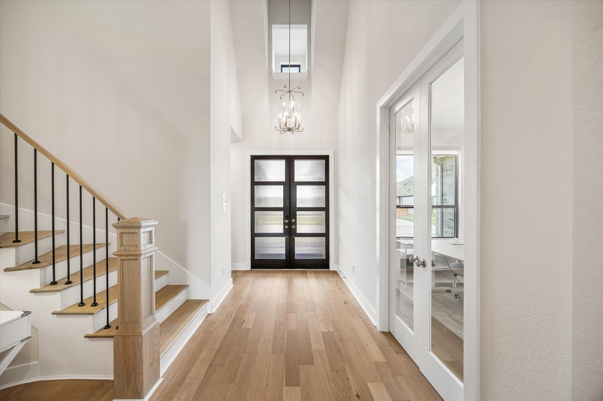 TWO-STORY FOYER WITH A STATEMENT CHANDELIER, MODERN DOUBLE FRONT DOORS, WOOD FLOORING, AND DIRECT ACCESS TO THE PRIVATE STUDY. TWO-STORY FOYER WITH A STATEMENT CHANDELIER, MODERN DOUBLE FRONT DOORS, WOOD FLOORING, AND DIRECT ACCESS TO THE PRIVATE STUDY.