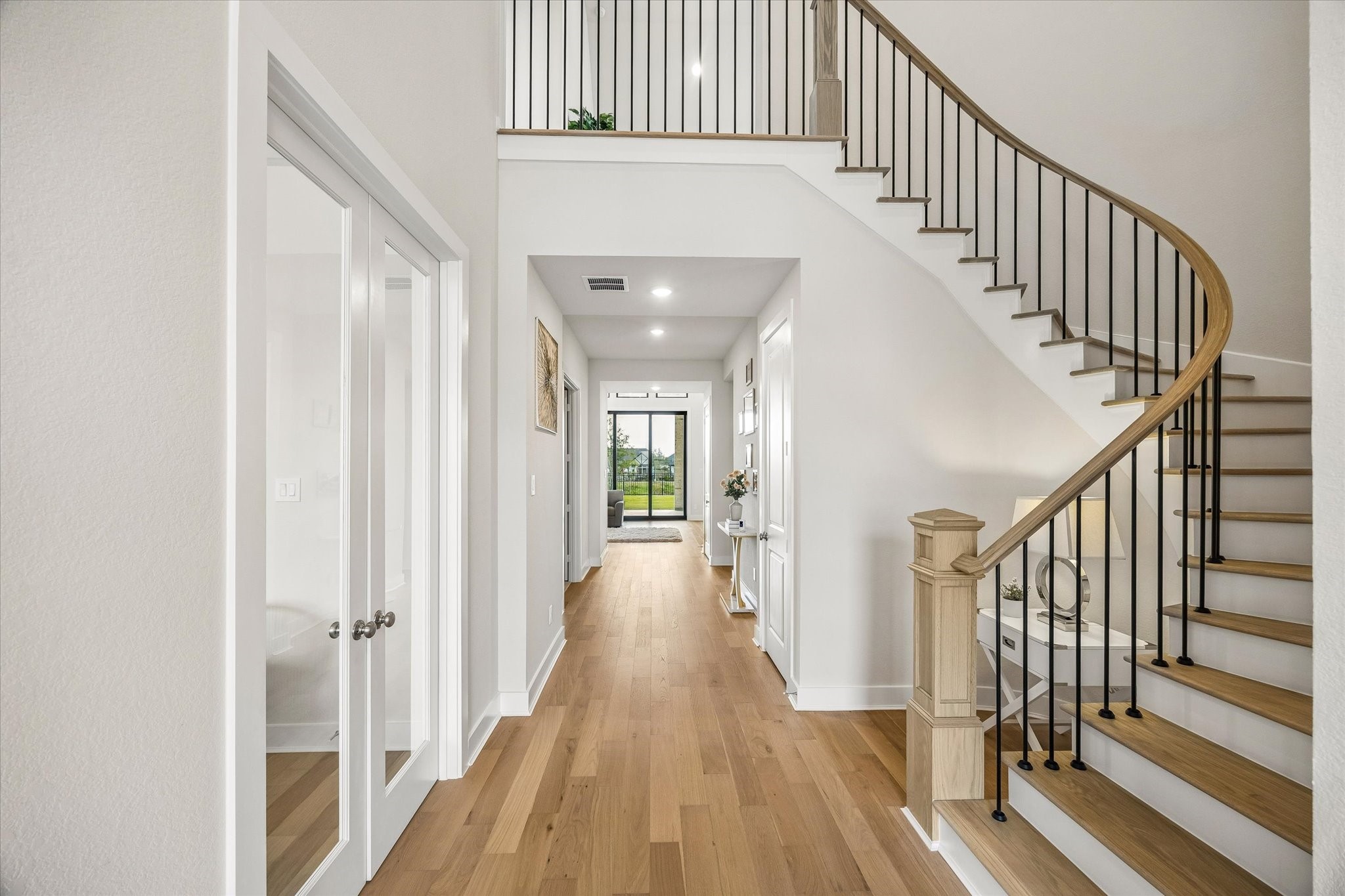 BRIGHT ENTRY HALL FEATURES WIDE-PLANK WOOD FLOORING AND A CURVED STAIRCASE WITH WOOD TREADS AND BLACK IRON BALUSTERS. BRIGHT ENTRY HALL FEATURES WIDE-PLANK WOOD FLOORING AND A CURVED STAIRCASE WITH WOOD TREADS AND BLACK IRON BALUSTERS.