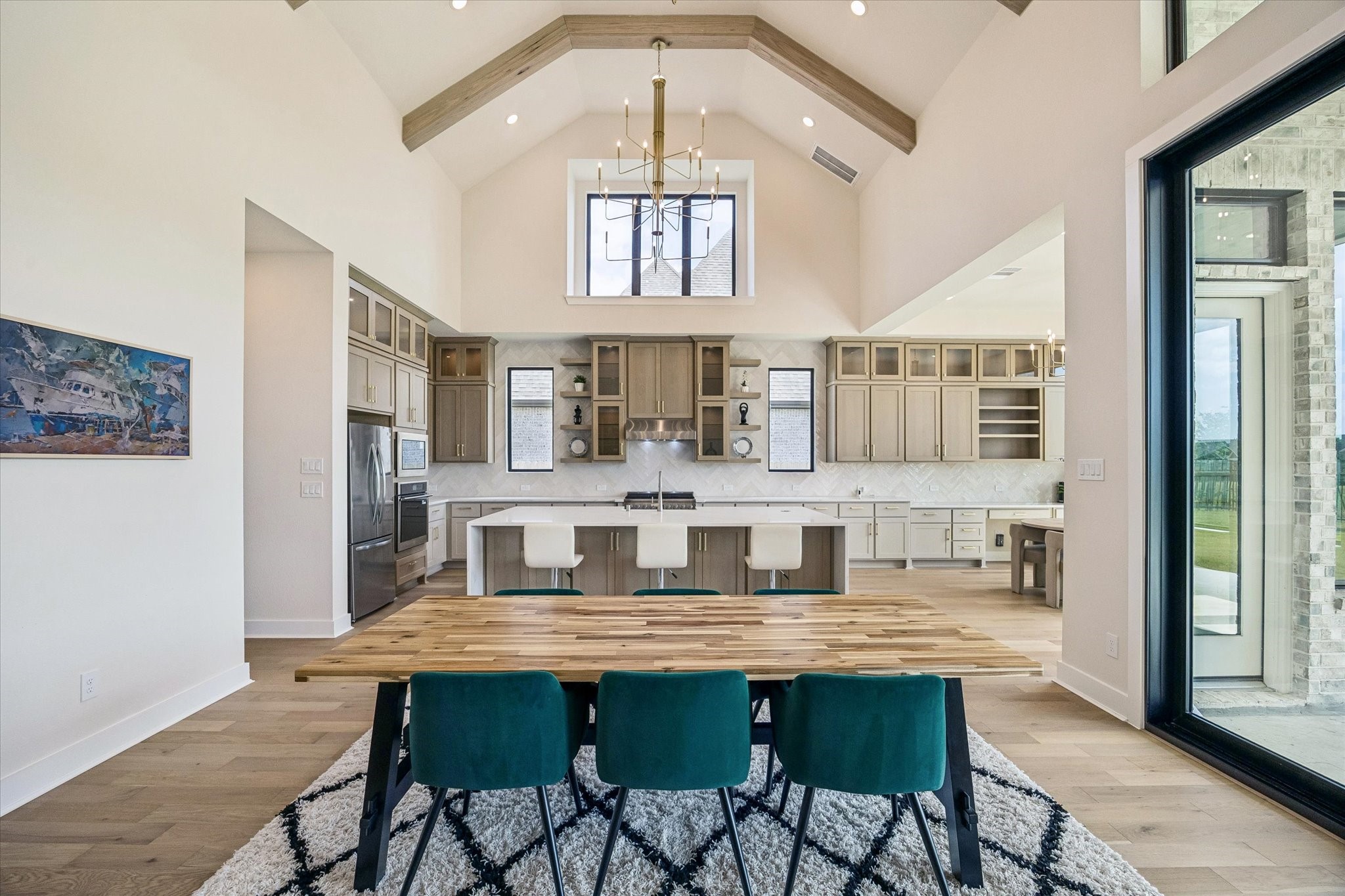 VAULTED CEILINGS AND EXPOSED WOOD BEAMS CREATE AN IMPRESSIVE BACKDROP FOR THE OPEN DINING AREA, WITH THE KITCHEN POSITIONED JUST BEYOND.