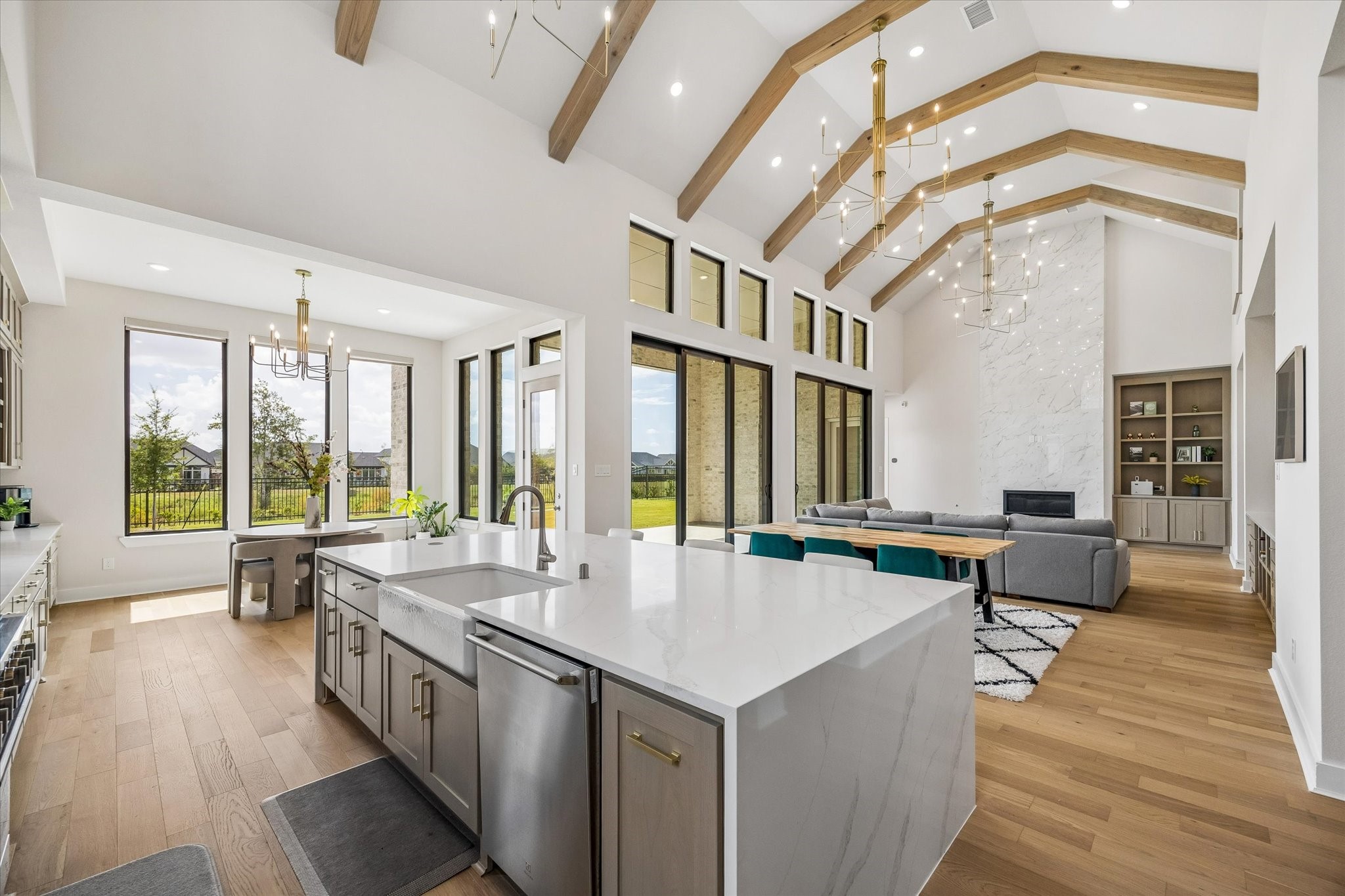 THIS VIEW HIGHLIGHTS THE SEAMLESS FLOW BETWEEN THE KITCHEN, BREAKFAST AREA, AND LIVING SPACE. A WALL OF TALL WINDOWS AND SLIDING GLASS DOORS BRINGS IN NATURAL LIGHT AND FRAMES THE BACKYARD.