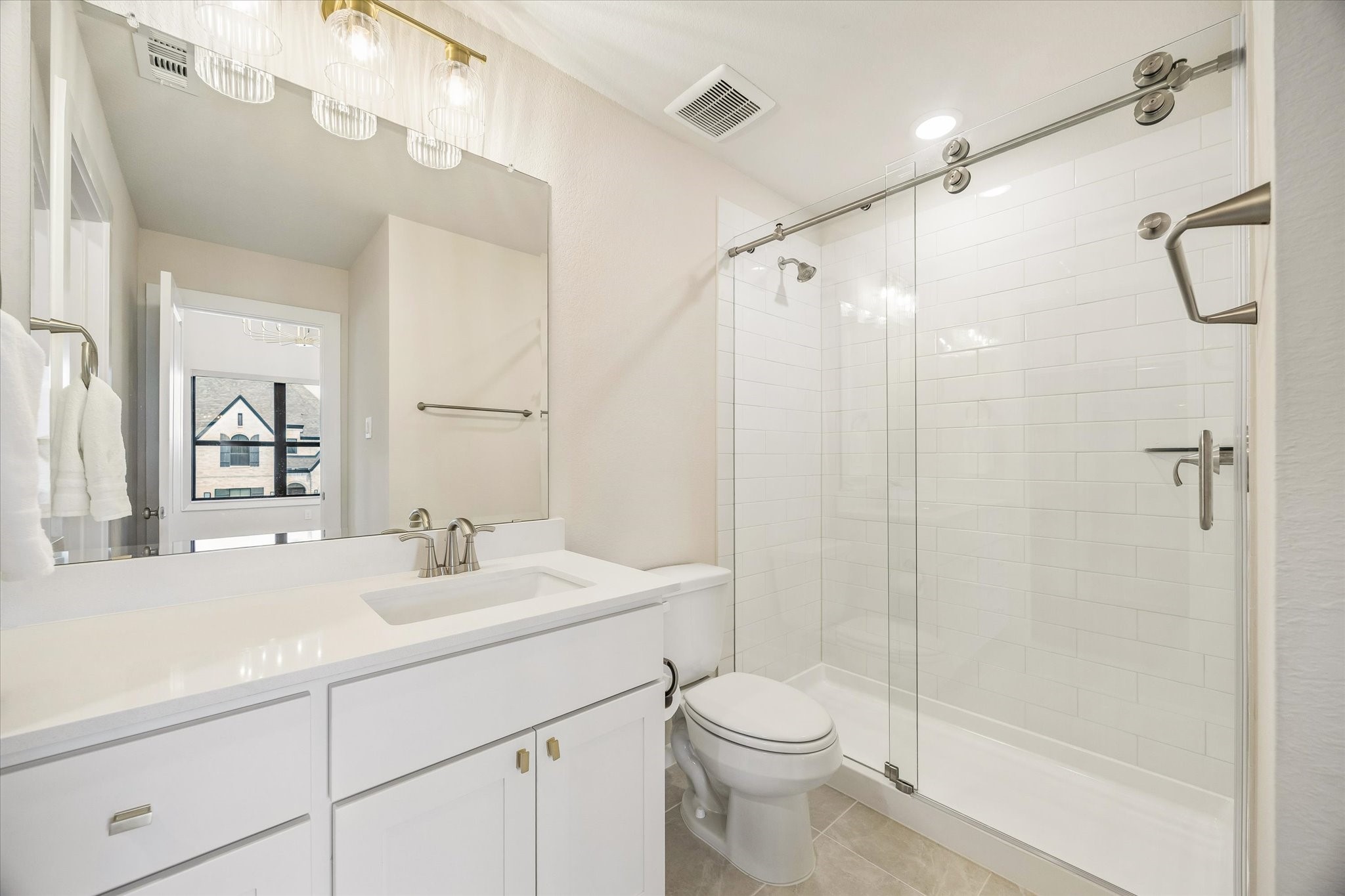 THIS SECONDARY BATH FEATURES A GLASS-ENCLOSED SHOWER, WHITE SUBWAY TILE, QUARTZ VANITY, AND CLEAN NEUTRAL FINISHES.
