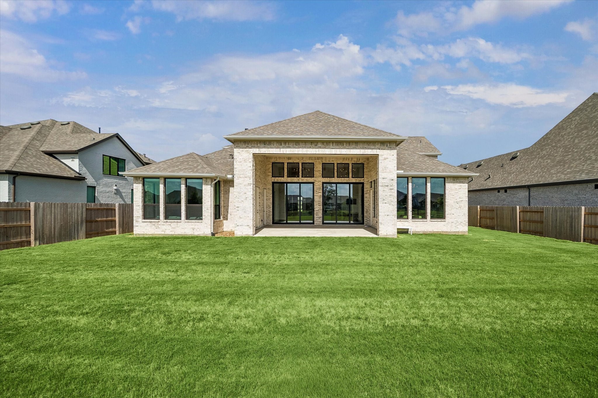 WIDE REAR VIEW SHOWCASES THE EXPANSIVE COVERED PATIO, MULTIPLE OVERSIZED WINDOWS AND SLIDING GLASS DOORS, AND A GENEROUSLY SIZED BACKYARD.