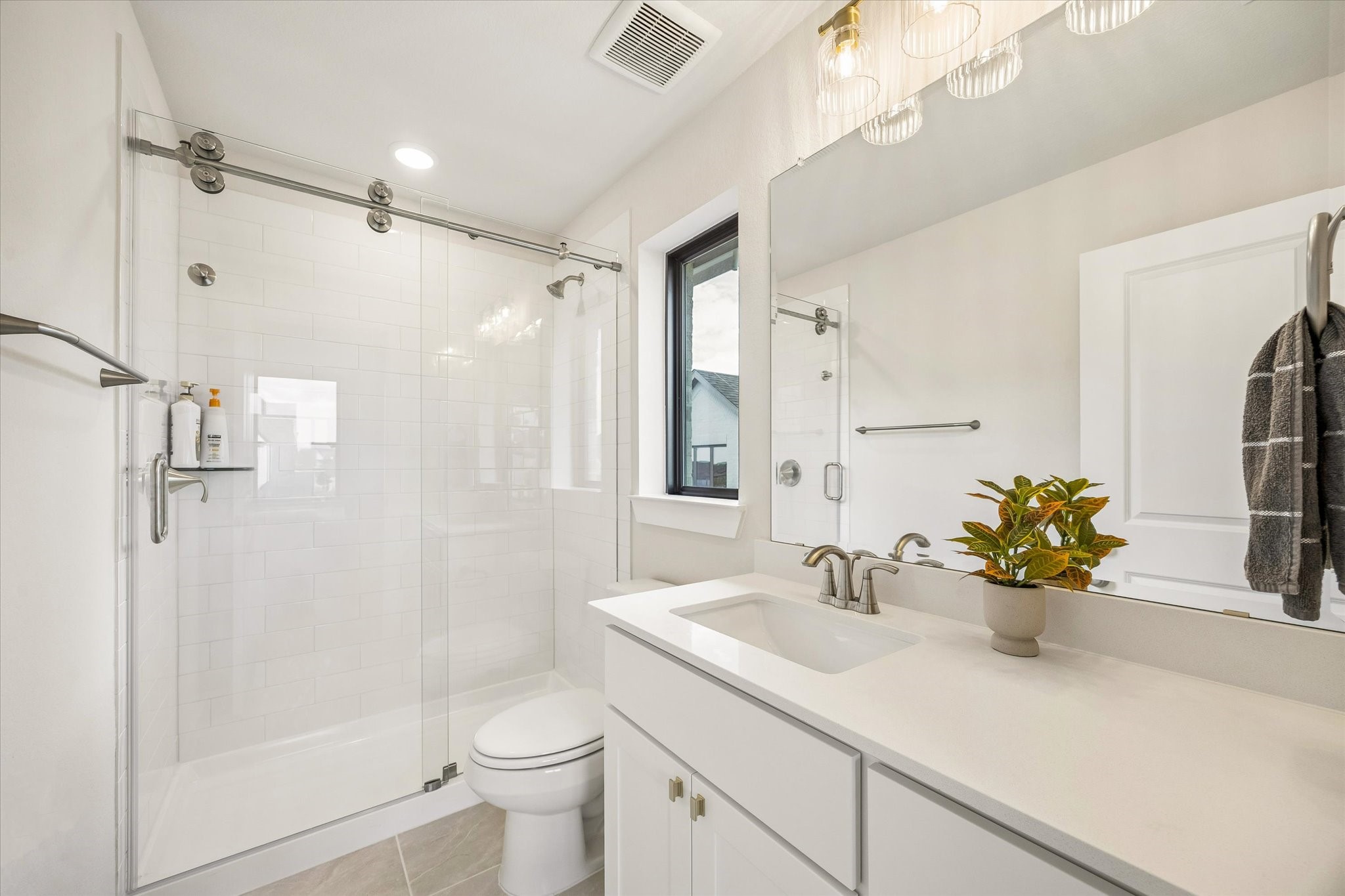 ANOTHER SECONDARY BATH OFFERS A WALK-IN SHOWER WITH FRAMELESS GLASS, SUBWAY TILE, QUARTZ COUNTERTOPS, AND A LARGE MIRROR.