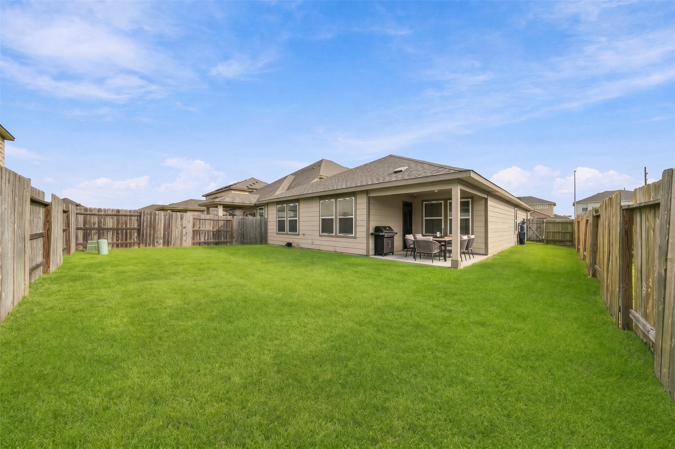 This photo captures a wide, eye-level, daytime outdoor view of a spacious residential backyard. The yard is entirely covered in a well maintained lush, vibrant green grass lawn.