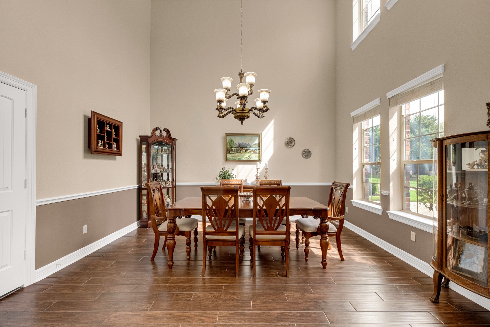 The formal dining room rises a full two stories, crowned by an ornate chandelier, with a chair-rail wainscot and a tall window bank that keeps the space bright without losing its formality.