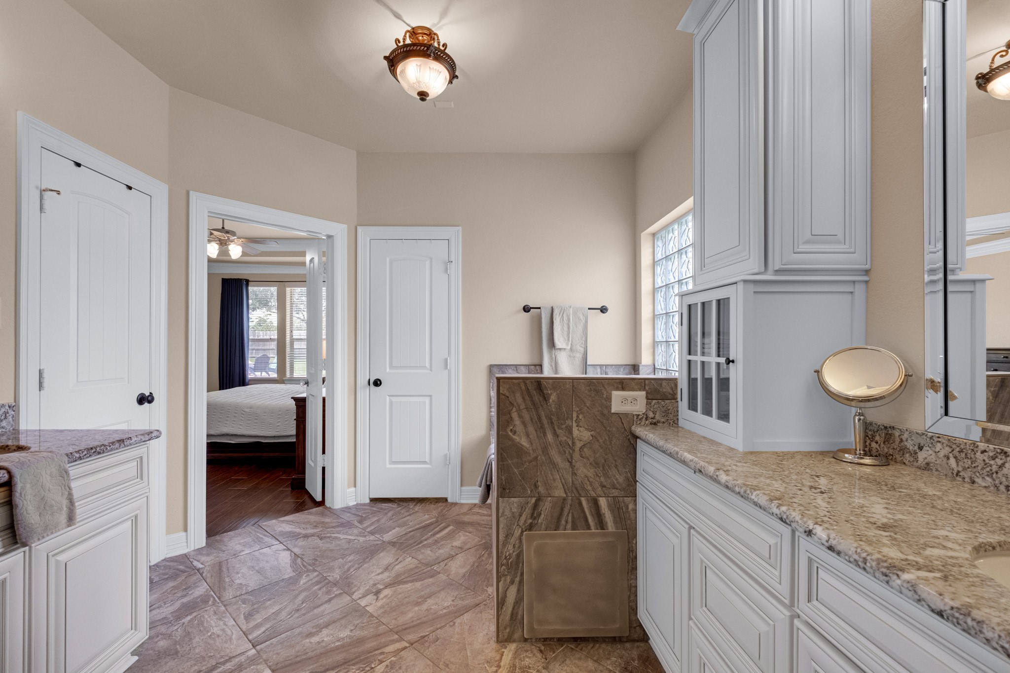 Travertine-look tile runs the floor and tub deck, with a linen tower, private water closet, and a direct door back to the bedroom.