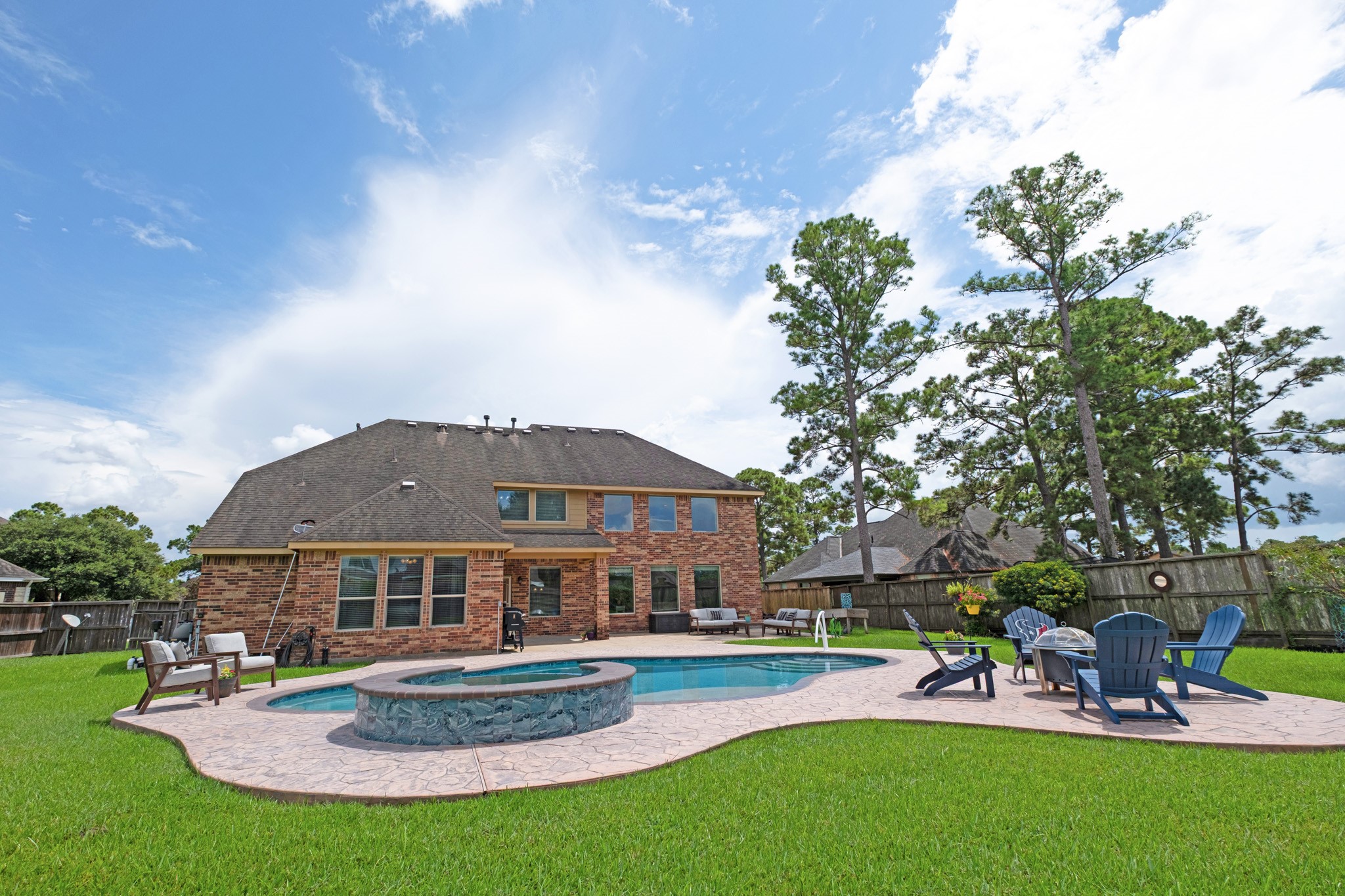 From the grass you see the whole rear composition: covered patio, pool, spa, and a fenced yard that keeps its distance from the neighbors.