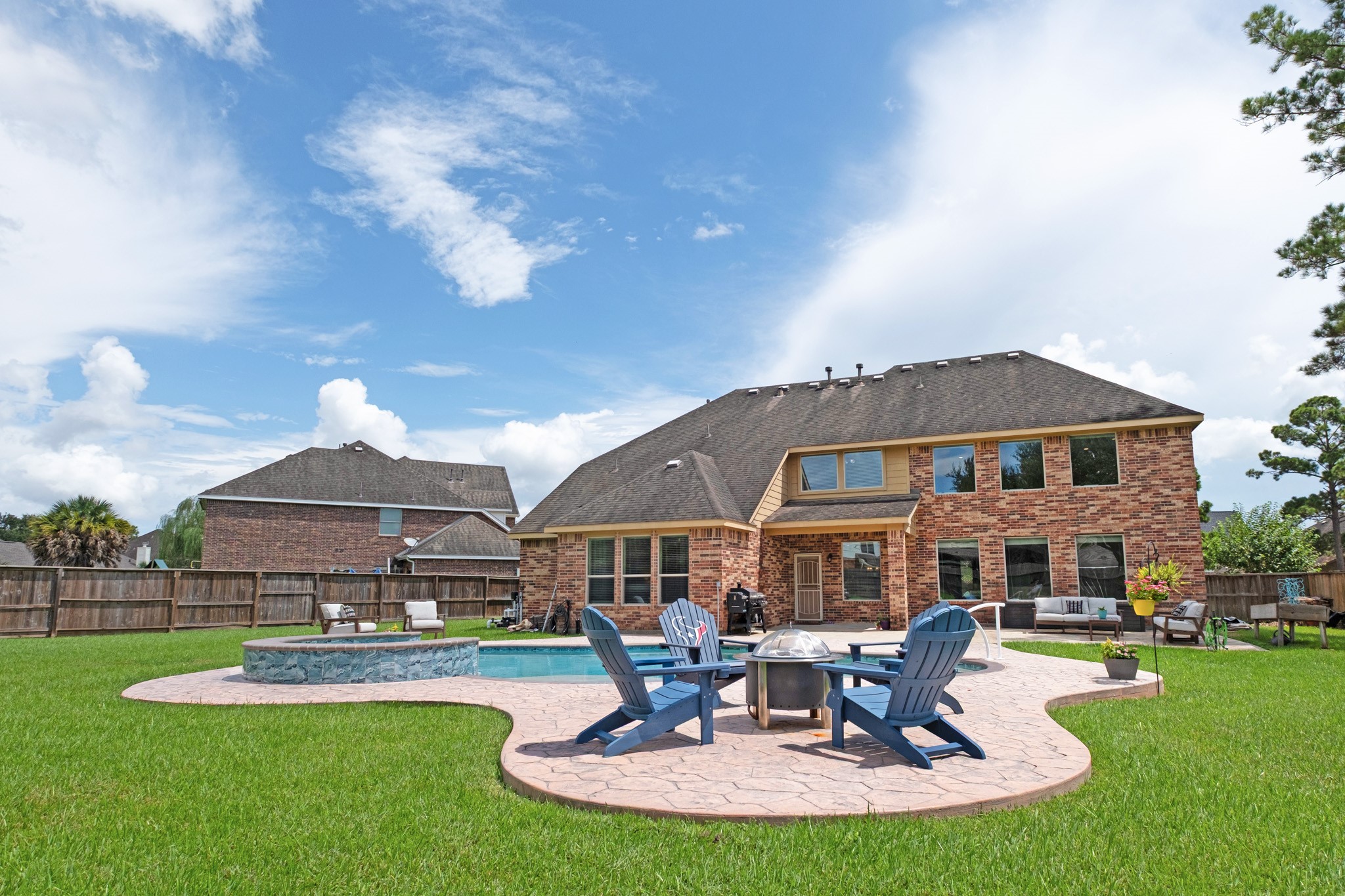 Out back, the story shifts to resort living - a freeform saltwater pool with a raised stone-faced spa, a sweeping stamped concrete deck, a fire pit gathering circle, and still a generous run of turf beyond the coping.