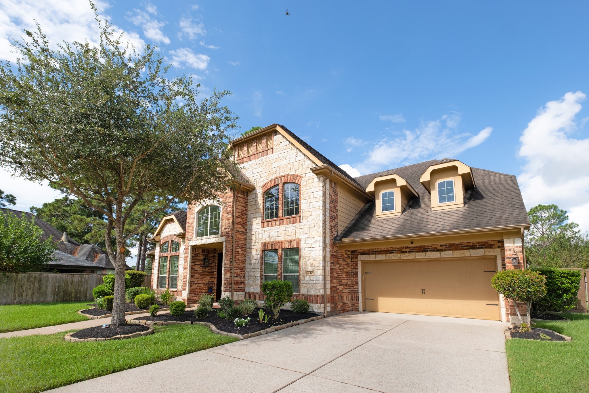 From the drive side you see the full massing: dormered roofline, brick-and-stone bay, and a wide approach that keeps parking off the cul-de-sac.