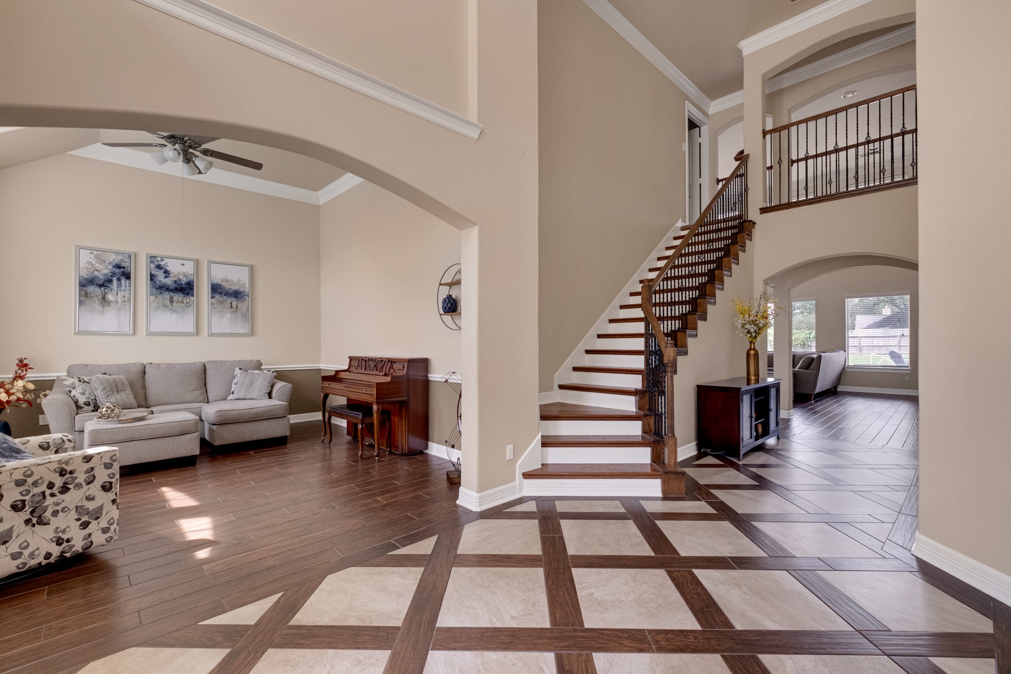 The foyer opens both directions at once - formal living through a soft arch to the left, the staircase and iron-railed catwalk to the right, and inlaid tile drawing the eye straight through.