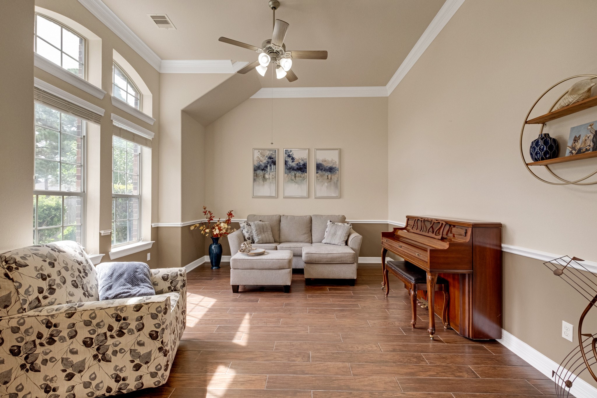 The formal living room lifts into a vaulted ceiling with crown molding, lit by tall arched windows and grounded by a two-tone wall treatment with chair rail.