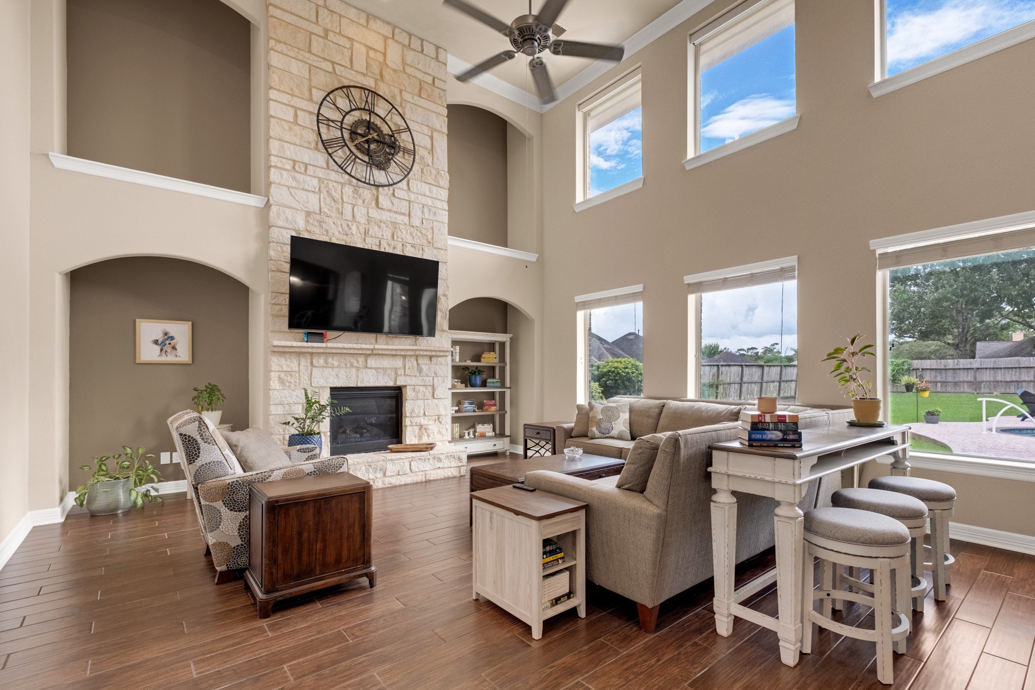 The family room reads best from the kitchen side: the stone chimney breast climbing to the ceiling, arched niches stacked on both walls, and clerestory windows above the main bank for a second layer of light.
