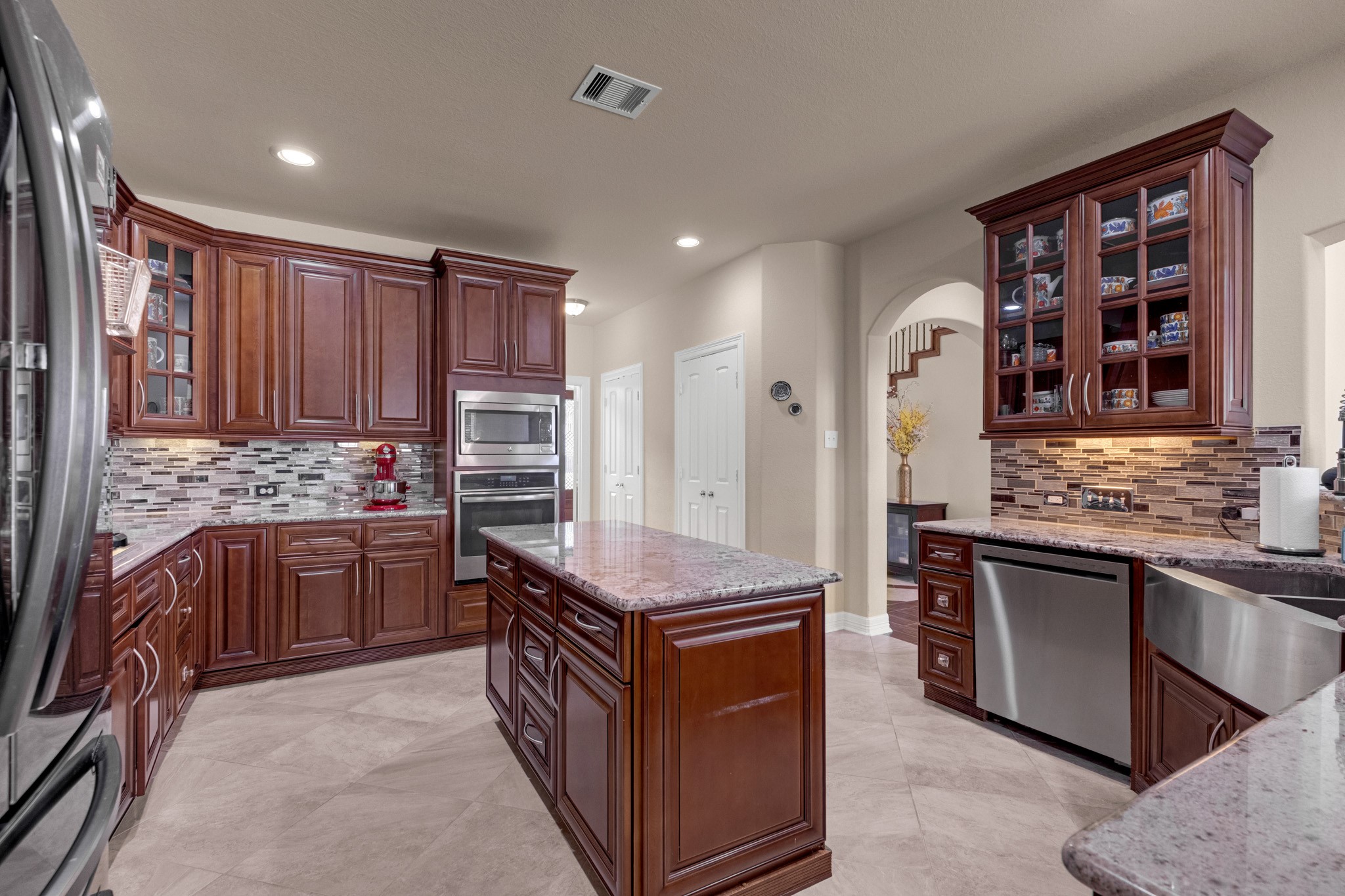 The kitchen works as hard as it looks - a granite-topped island, glass-front display uppers, undercabinet lighting, stainless dishwasher, and a coffee-bar run tucked against the breakfast side.