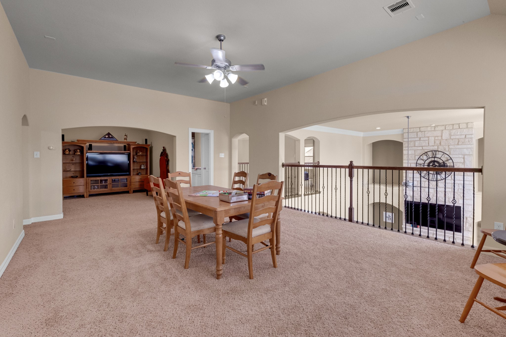 The upstairs game room opens over an iron-railed overlook to the family room below, with a media wall and room for a full-size table alongside.