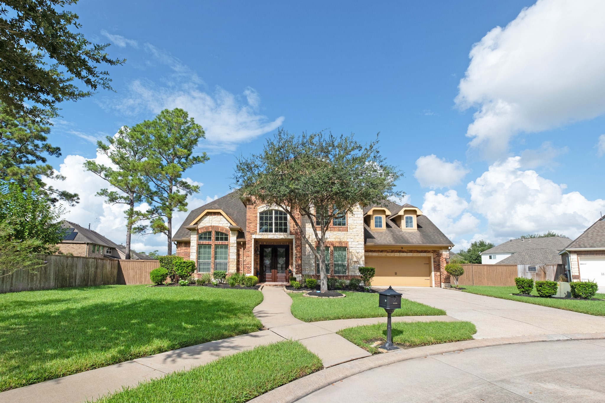 Head-on, the symmetry comes together - steep gables over the stone-faced entry, twin dormers stepping down toward the garage, and an oversized drive with room to turn.