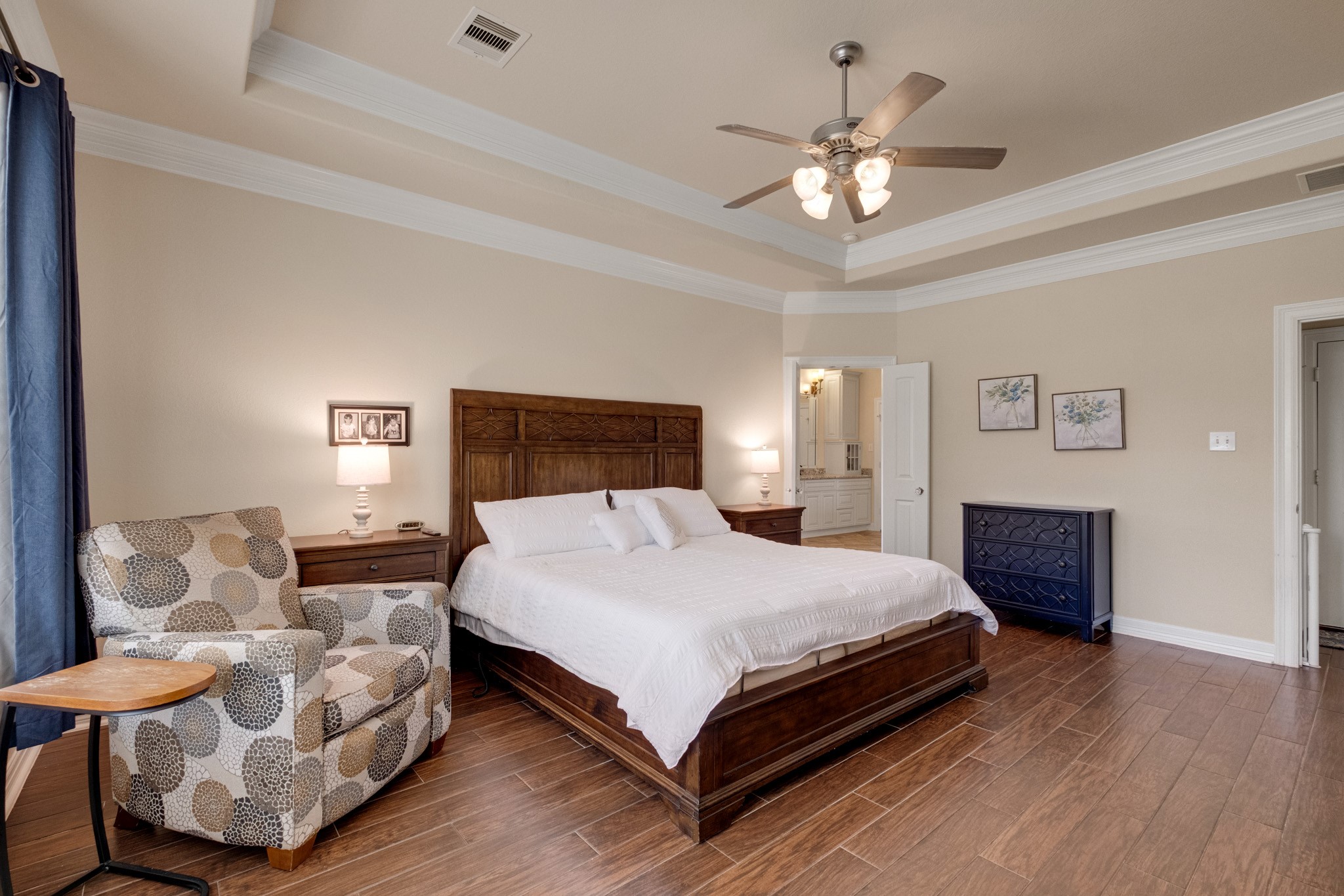 From the doorway, the primary suite reads generously - tray ceiling with crown, ensuite framed in the corner, and enough room for a king plus a sitting area.