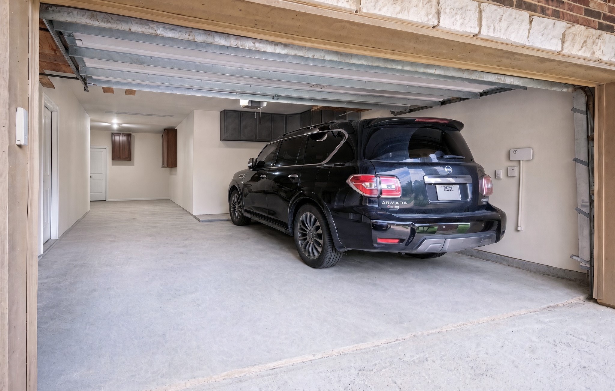 That is a full-size SUV in the right-hand bay, and it fits with room to spare - the clearest measure of how deep and wide this attached three-car tandem garage runs. The tandem bay beside it still takes a third vehicle, a workshop bench, or the lawn equipment, with overhead cabinet storage and direct interior access.