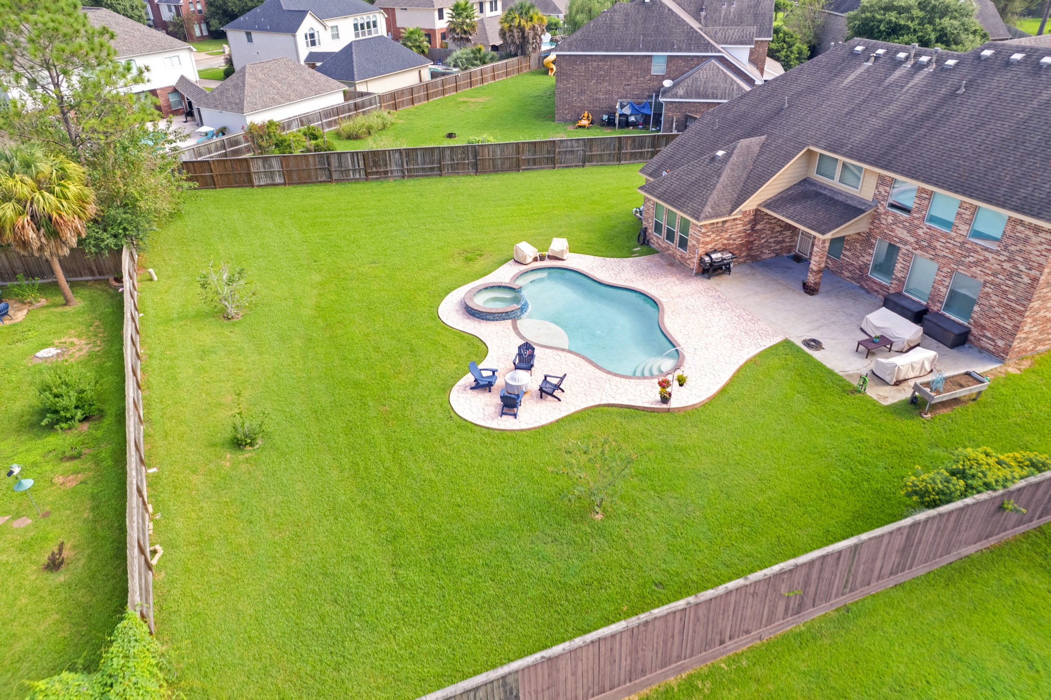 From above, the pool and deck read as a single sculpted shape set into a deep, fully fenced half-acre lot with room to spare in every direction.