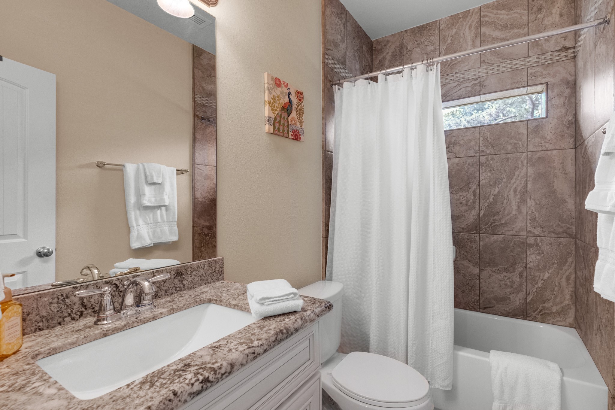 A secondary full bath carries the finishes through - large-format tile tub surround with mosaic accent band, granite-topped vanity, and a privacy window over the tub.