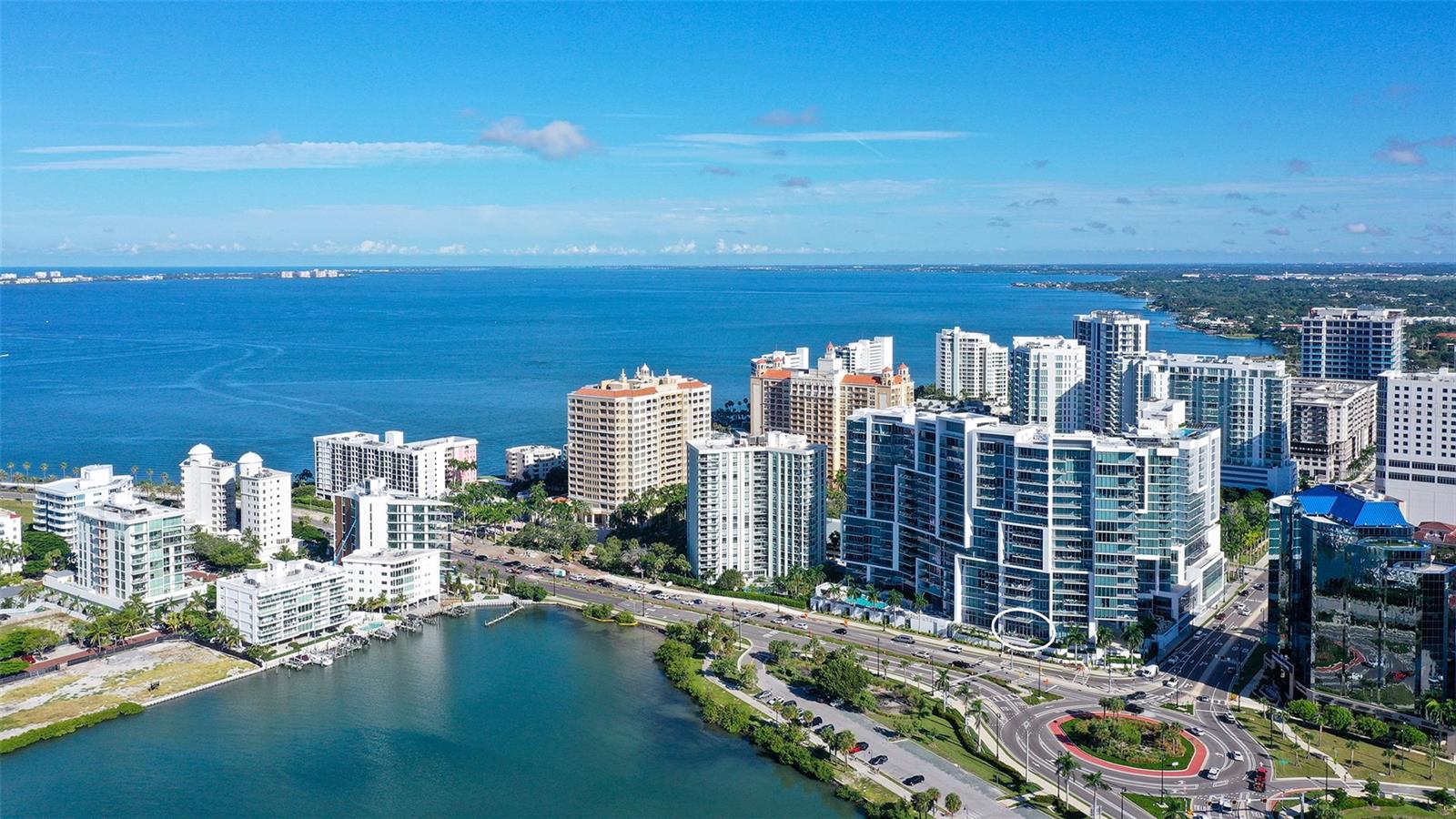 An aerial view showcases The VUEs iconic waterfront architecture overlooking the sparkling waters of Sarasota Bay toward Longboat Key.