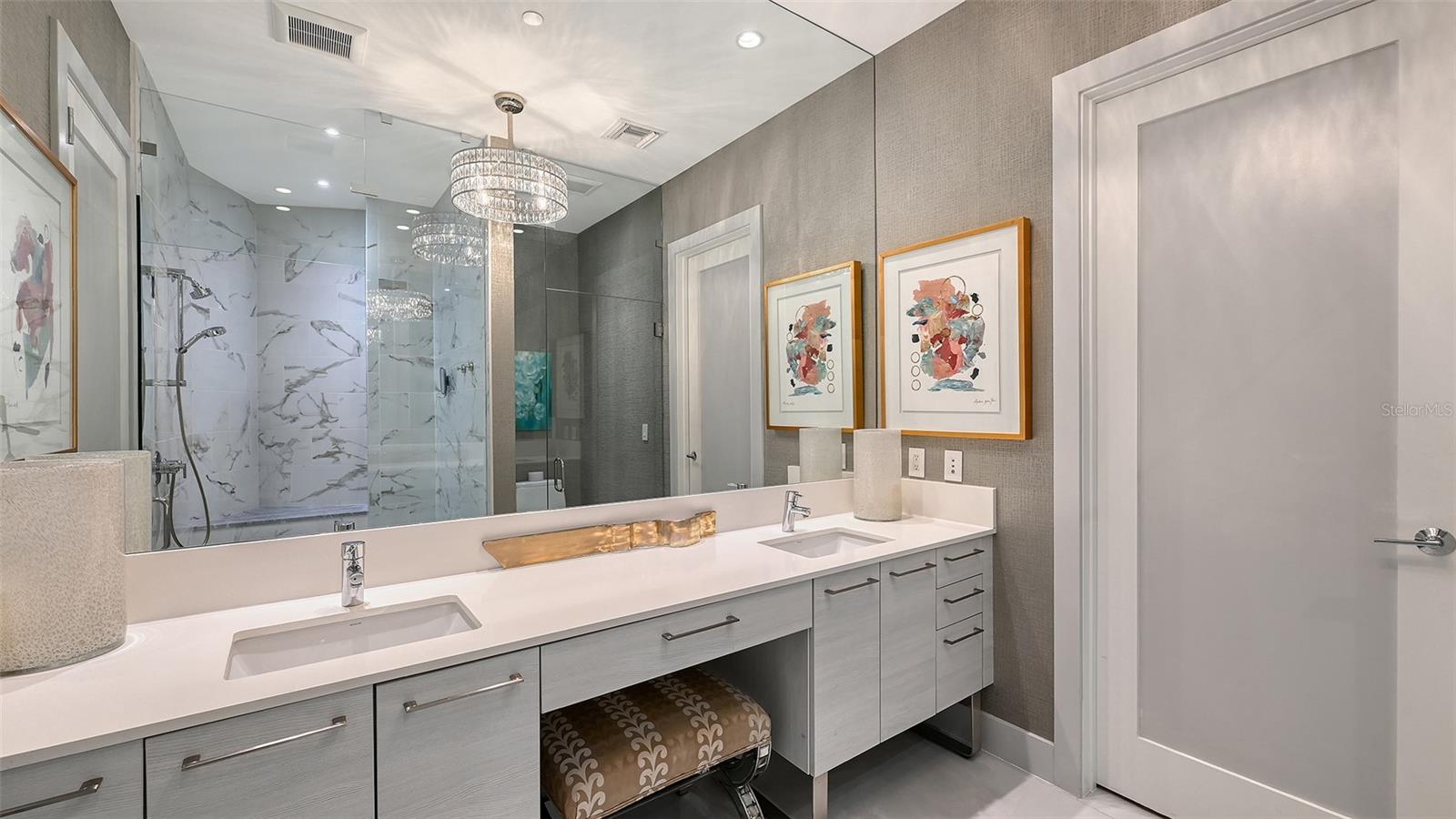 An elegant primary bath featuring dual sinks, a dedicated makeup vanity with an oversized mirror, and a custom chandelier for a touch of refined luxury.