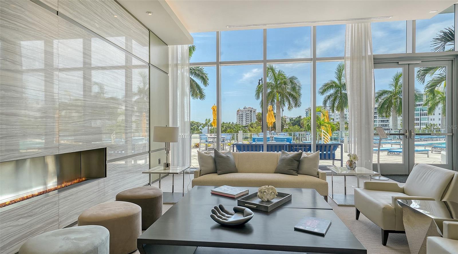 An elegant lobby seating area framed by floor-to-ceiling windows overlooking the resort-style pool, offering a bright, inviting space to relax and enjoy the view.