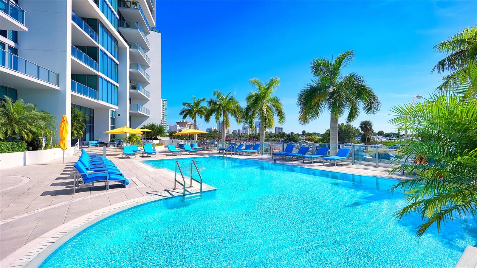 A sparkling blue resort-style pool surrounded by an elegant sun deck with inviting lounge chairs and umbrellas, creating the perfect setting for relaxation and soaking up the Florida sunshine.
