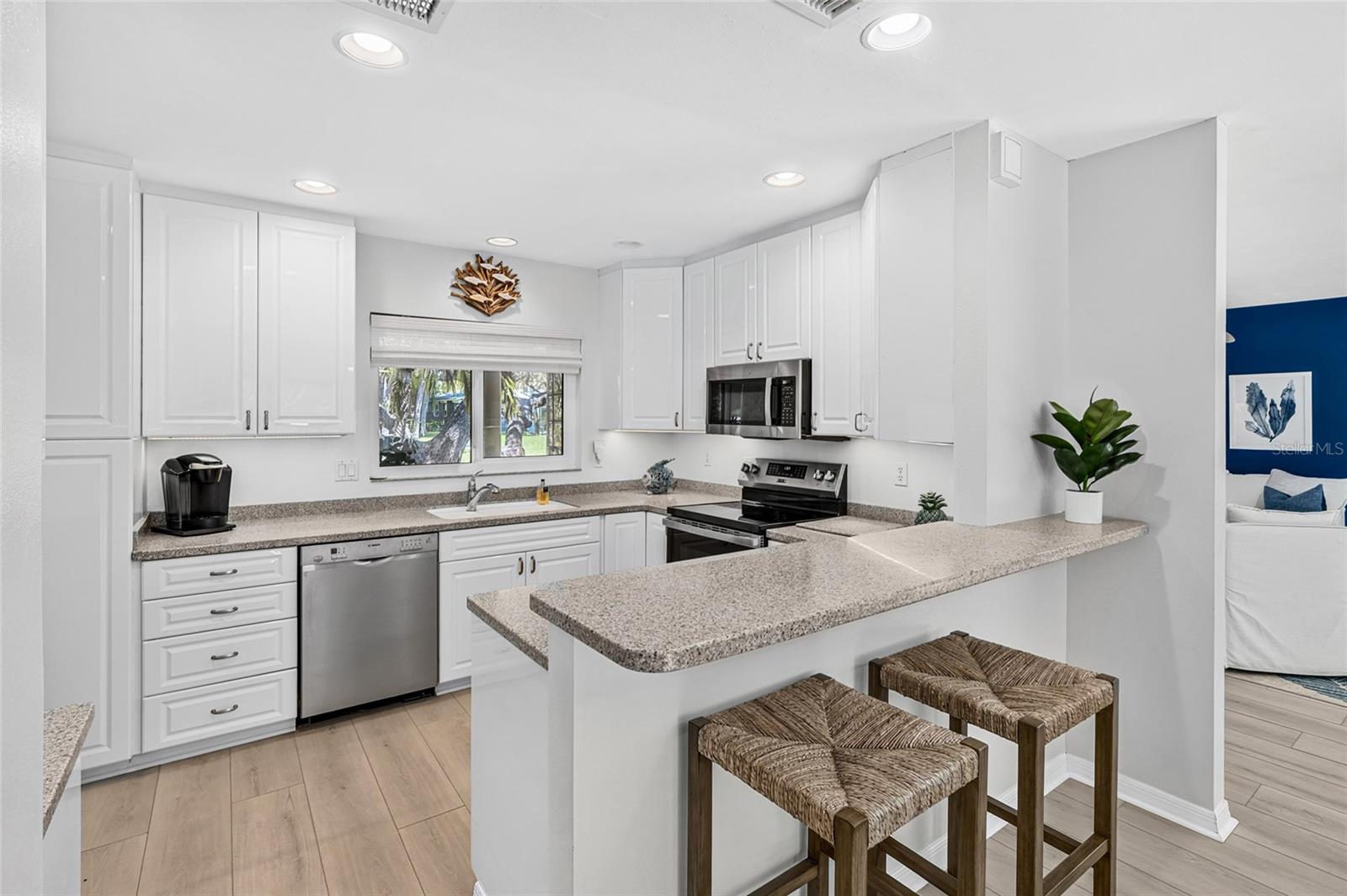 Bright white kitchen offers generous cabinetry, stone counters, stainless appliances and plenty of gathering space.