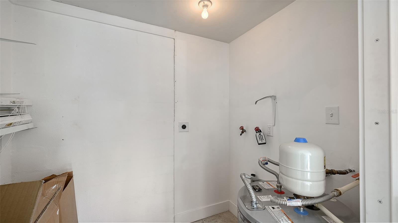 The storage room behind the carport with the new water heater and previous washer/dryer hookup.