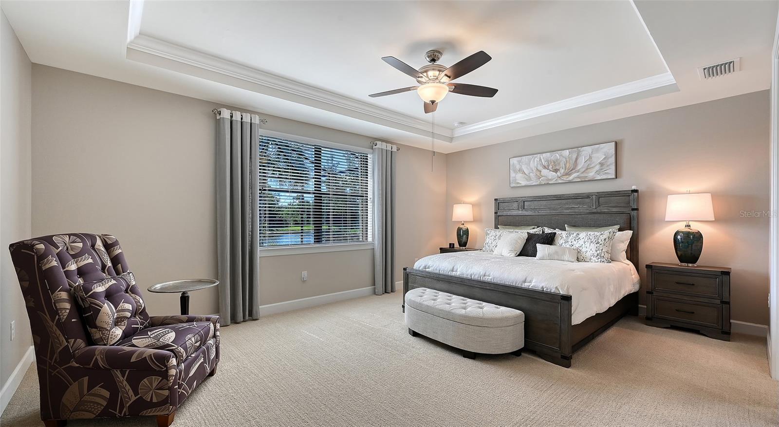 This spacious primary suite features an elegant tray ceiling and captivating views of the sparking pool and picturesque water beyond.
