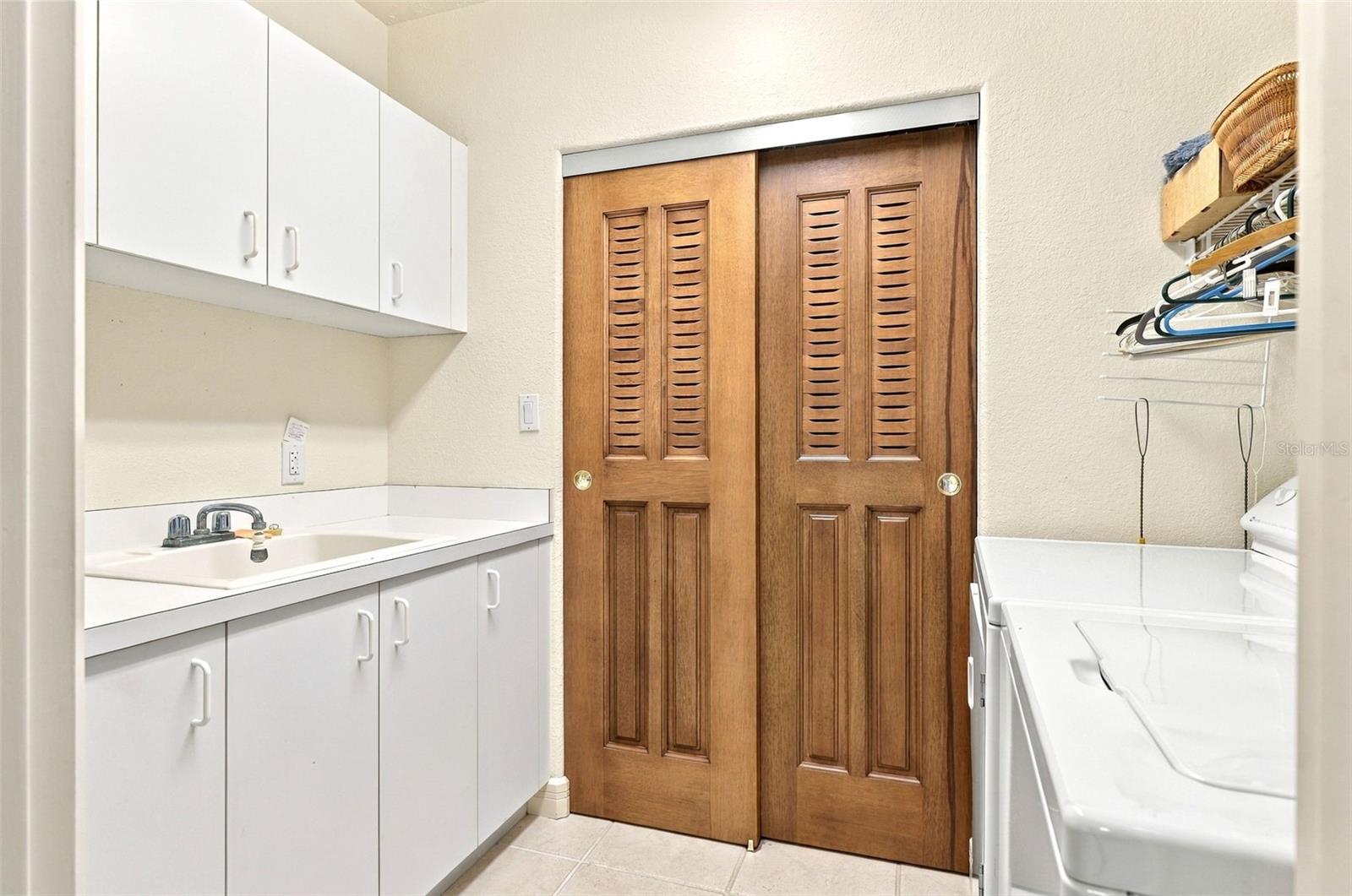 In unit laundry with fitted cabinetry, laundry tub, and utility closet.