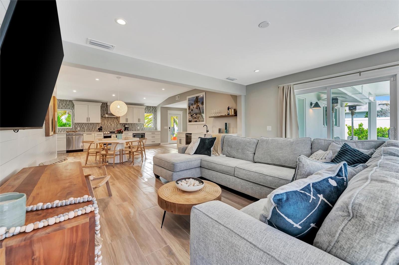 Walls of windows showcase canal views, heated saltwater pool, covered lanai, outdoor terraces, built-in grill, and tiki hut with turf games area.