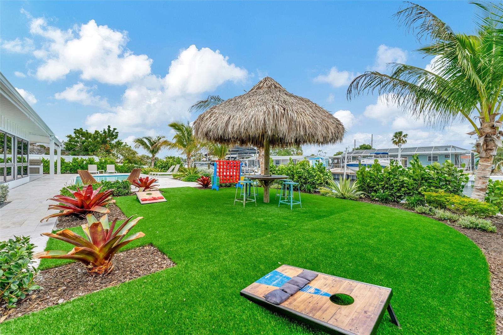 Covered lanai, multiple terraces, built-in propane grill, and tiki hut with turf games area.