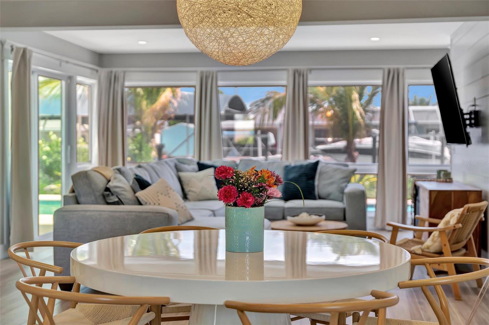 Walls of windows showcase canal views, heated saltwater pool, covered lanai, outdoor terraces, built-in grill, and tiki hut with turf games area.