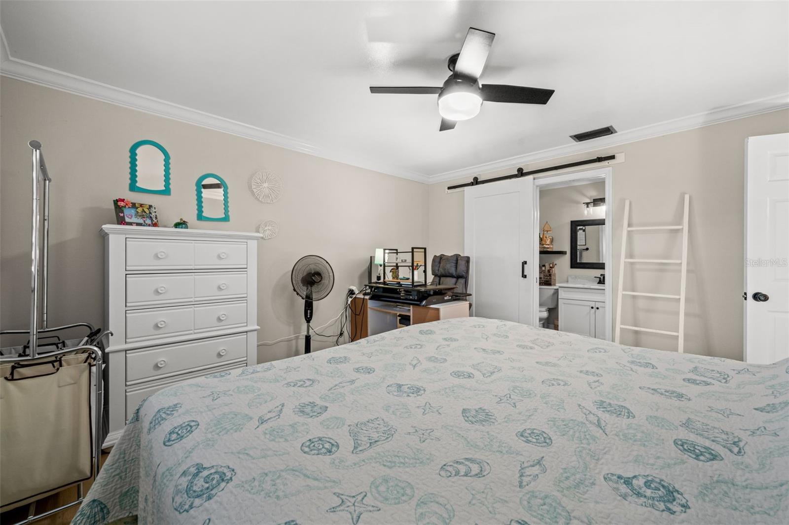 A large primary bedroom featuring a ceiling fan with integrated lighting and barn door entry to the ensuite and walk-in closet.