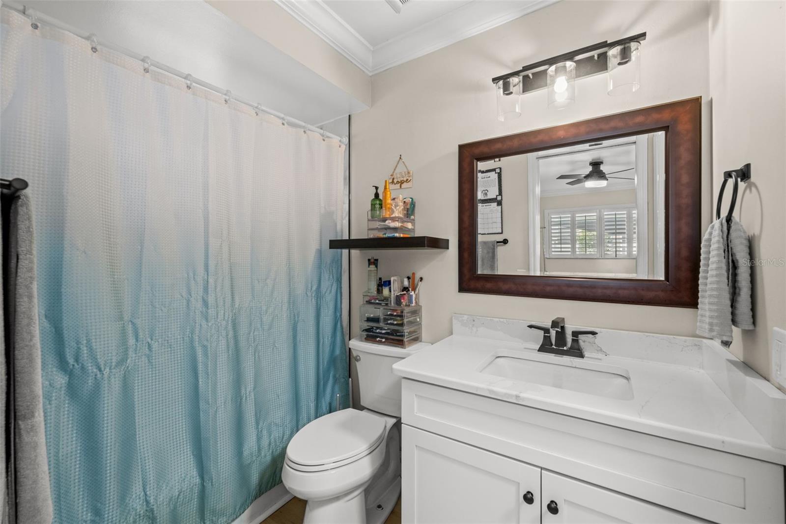Notice the rectangular undermount sink, the dark-finish faucet, the framed mirror, and the three-light wall fixture.
