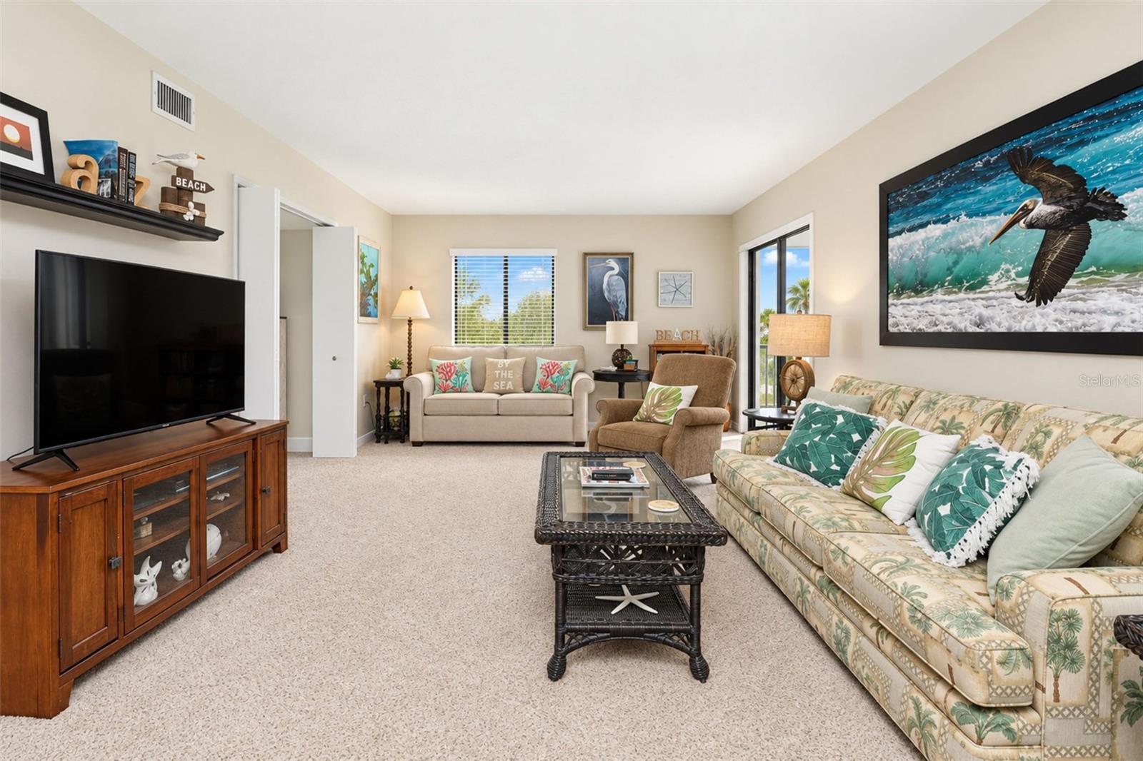 The living room has carpeted flooring and sliding glass doors to the lanai. The living room has carpeted flooring and sliding glass doors to the lanai.