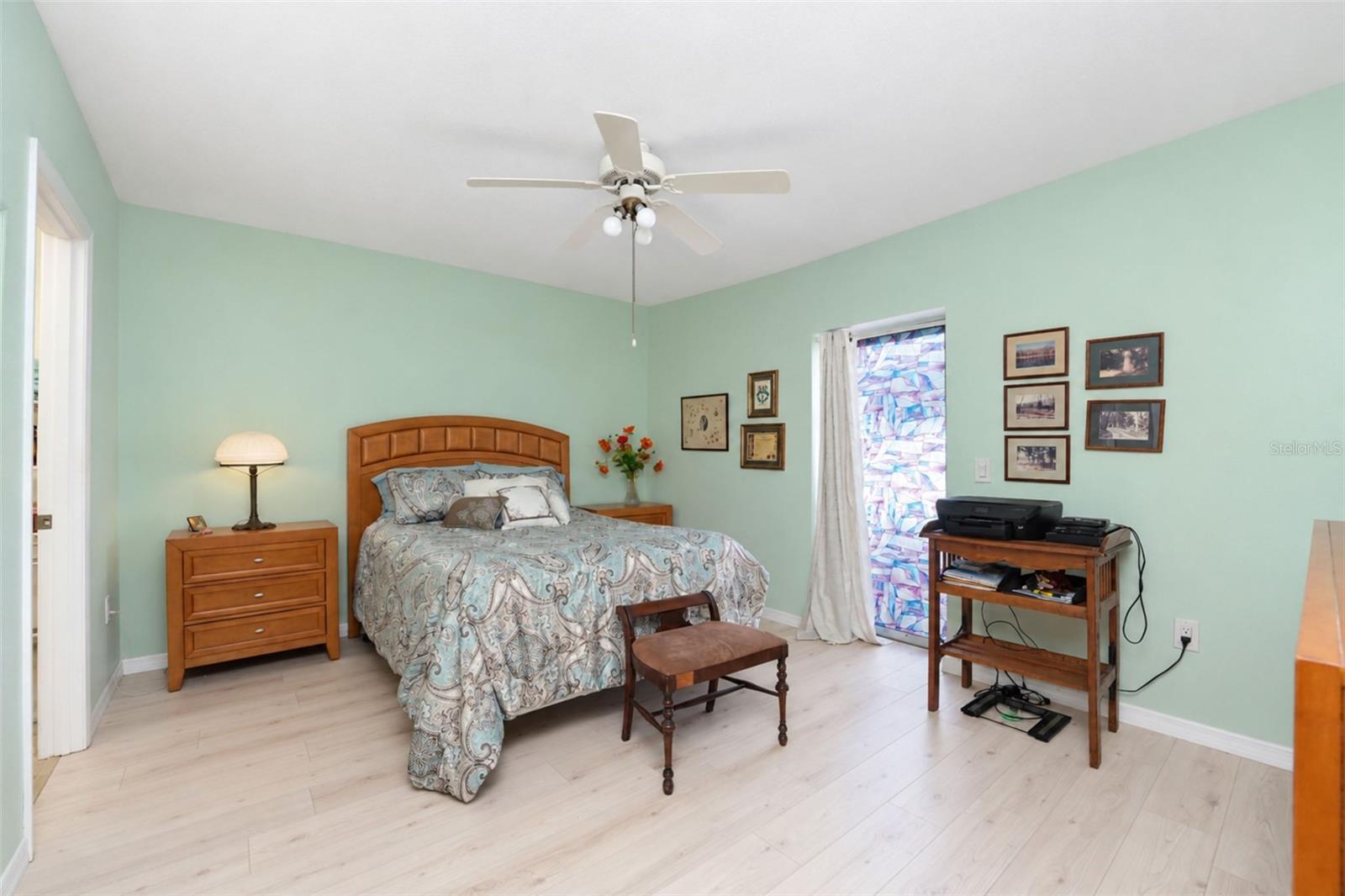 The primary bedroom features wood laminate flooring, a ceiling fan and sliding glass doors to the rear patio.