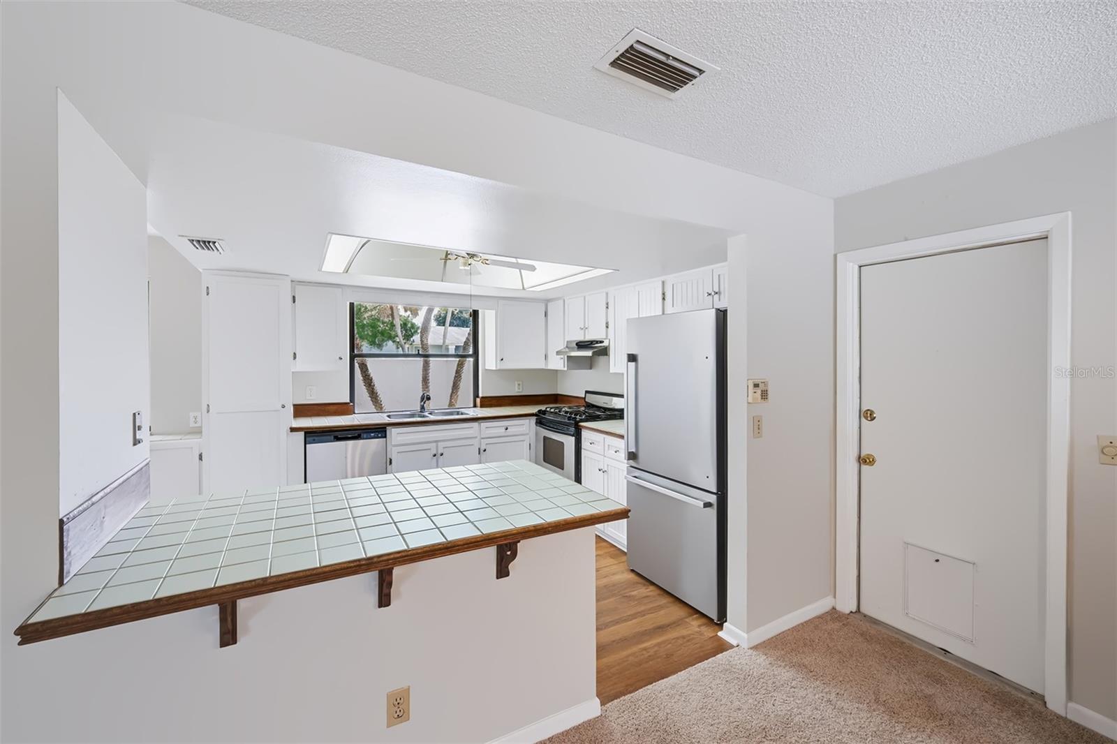 View into the kitchen from the dinette area/small breakfast bar. Garage door to the right with doggie door