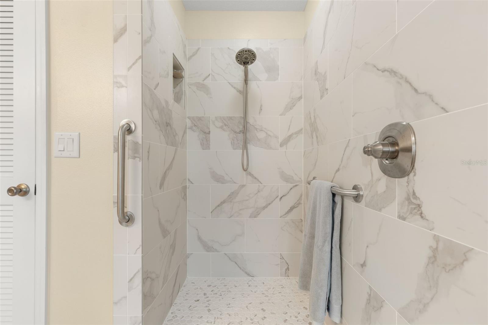A closer look at the beautifully updated primary shower reveals striking tile, a pebble-style floor, built-in niche, and handheld showerhead, creating a refreshing escape with a touch of modern elegance.