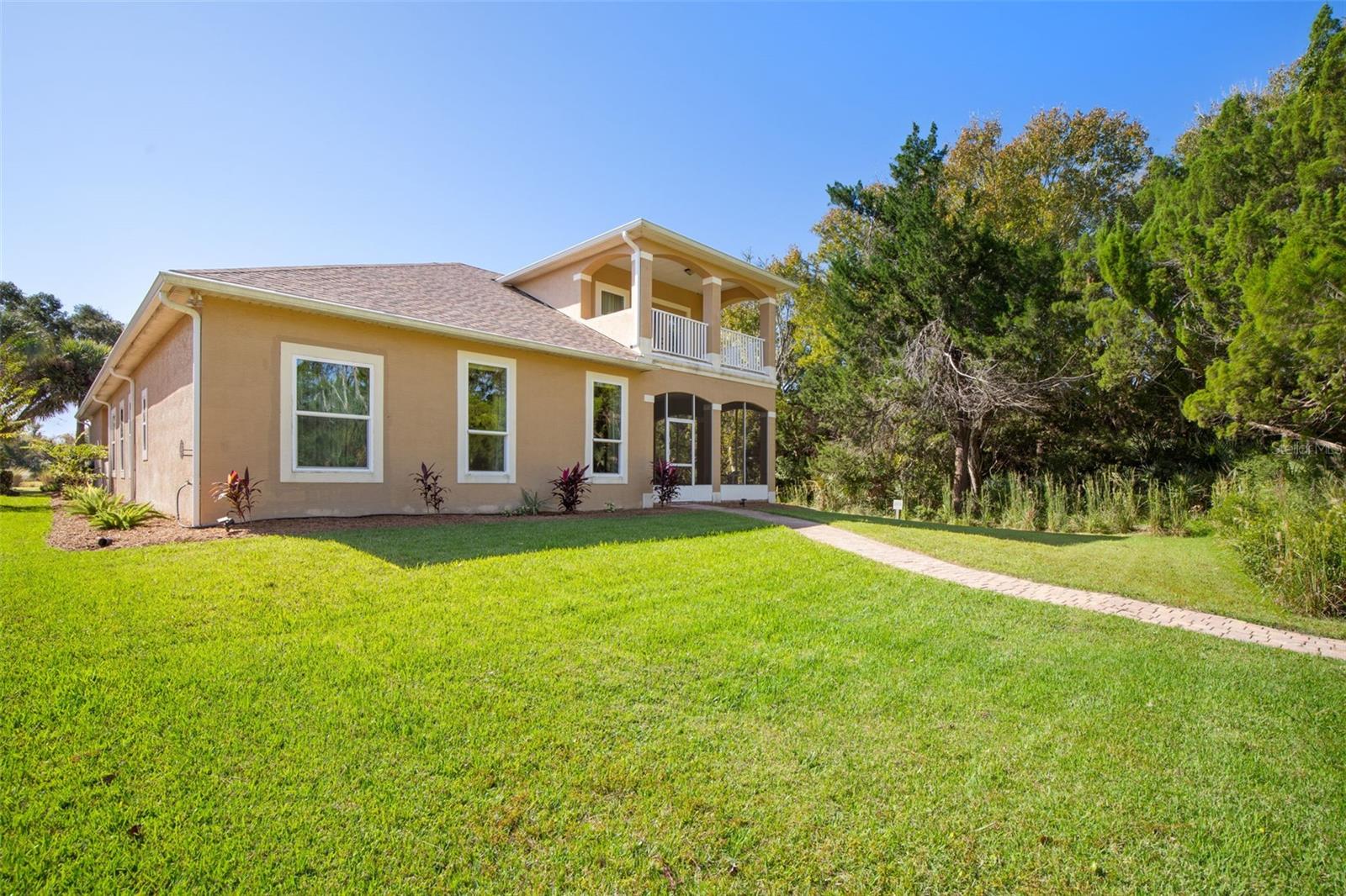 Rear exterior featuring a private upstairs balcony, screened lanai, and spacious backyard.
