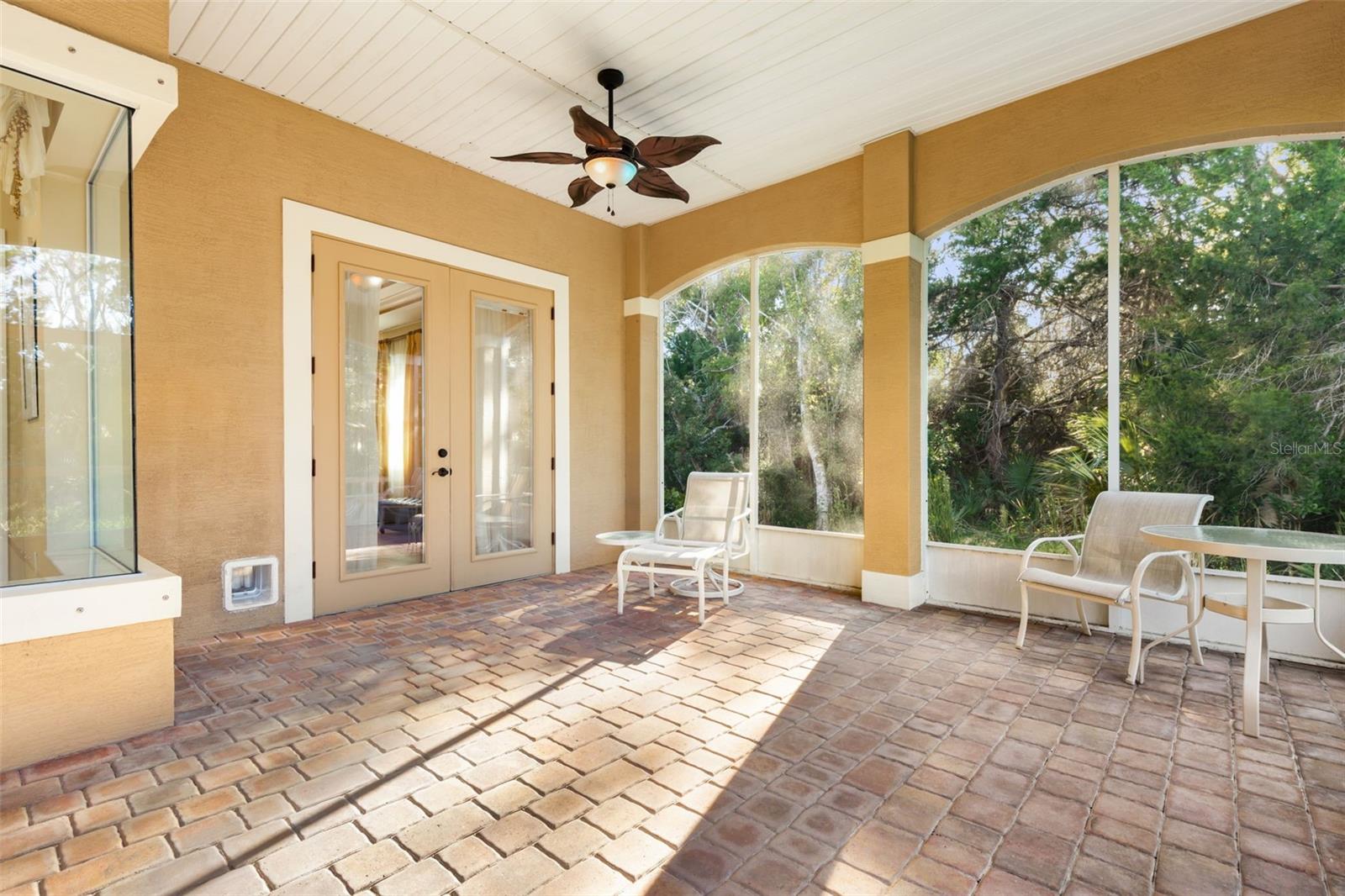 Screened lanai with paver flooring and French doors leading to the first-floor primary suite.