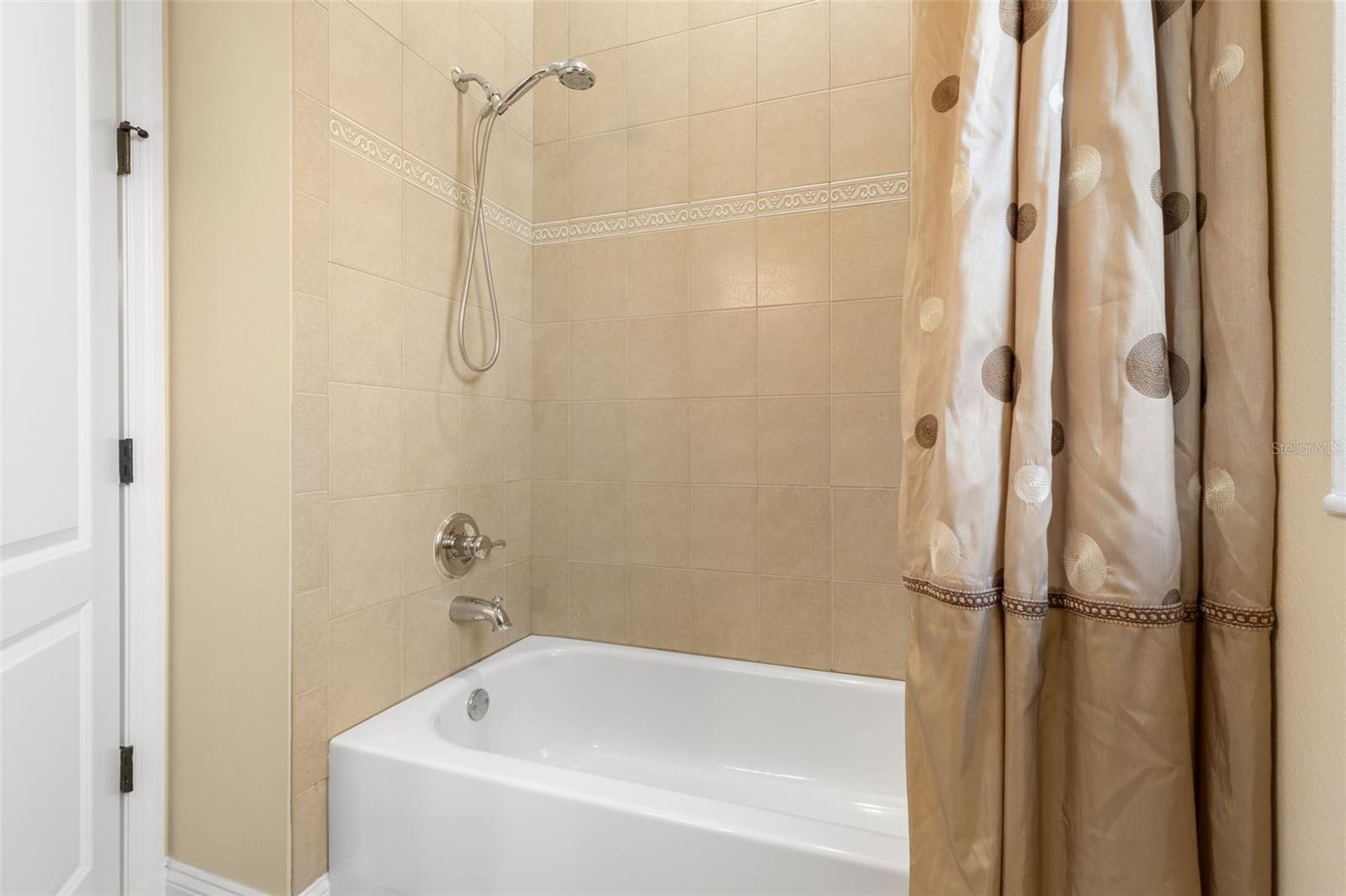 A closer look at the first-floor guest bathroom's tub/shower combination, featuring decorative tile accents and a handheld showerhead.