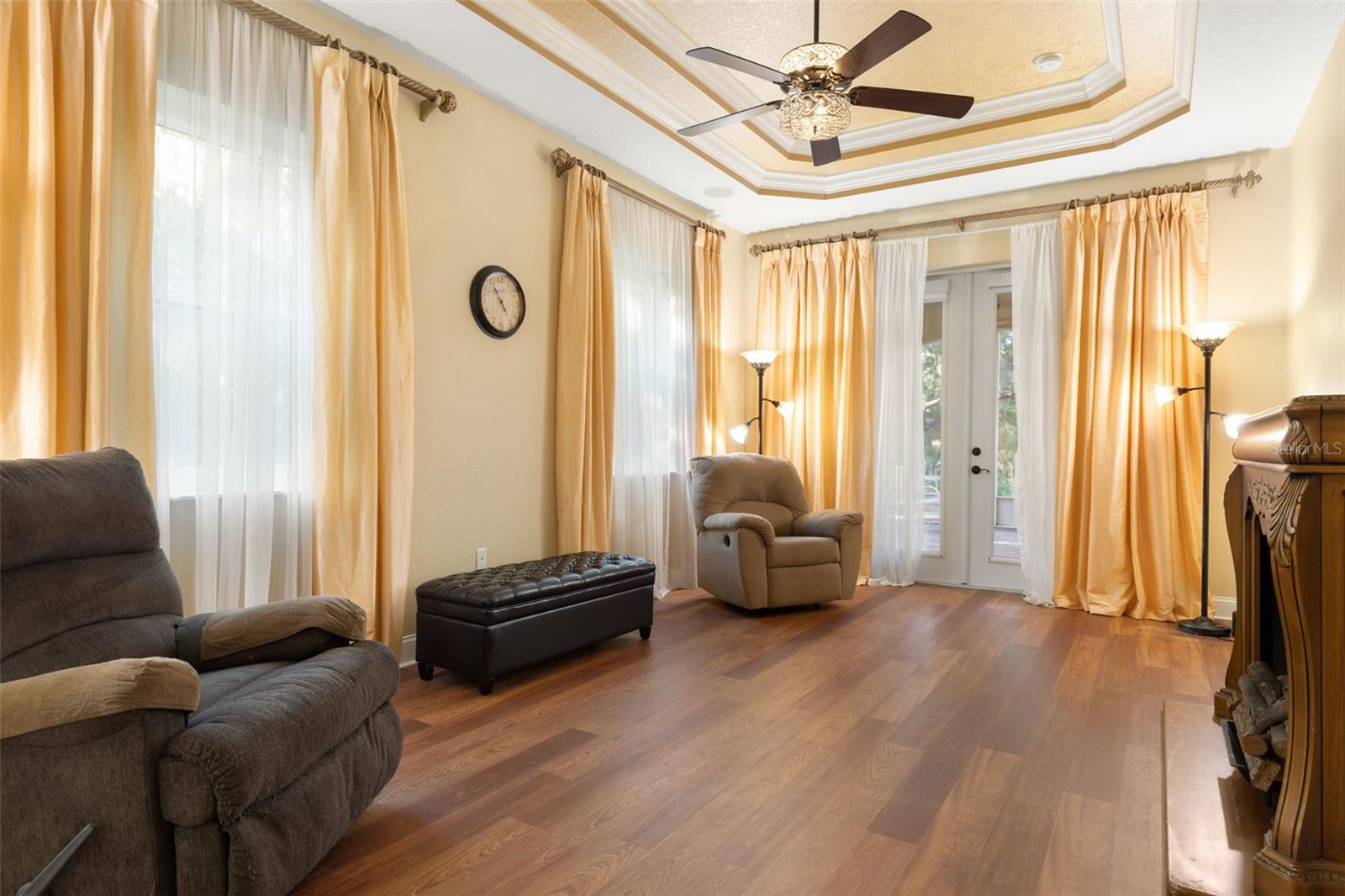 A spacious first-floor primary retreat featuring an elegant tray ceiling, abundant natural light and French doors opening to the screened lanai.