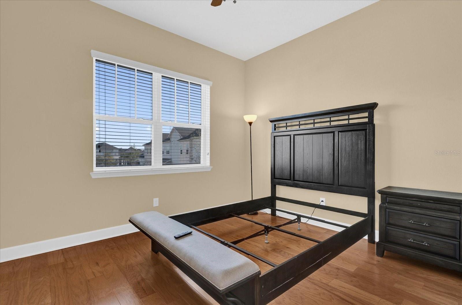 Comfortable third bedroom with rich hardwood flooring and a bright window view.