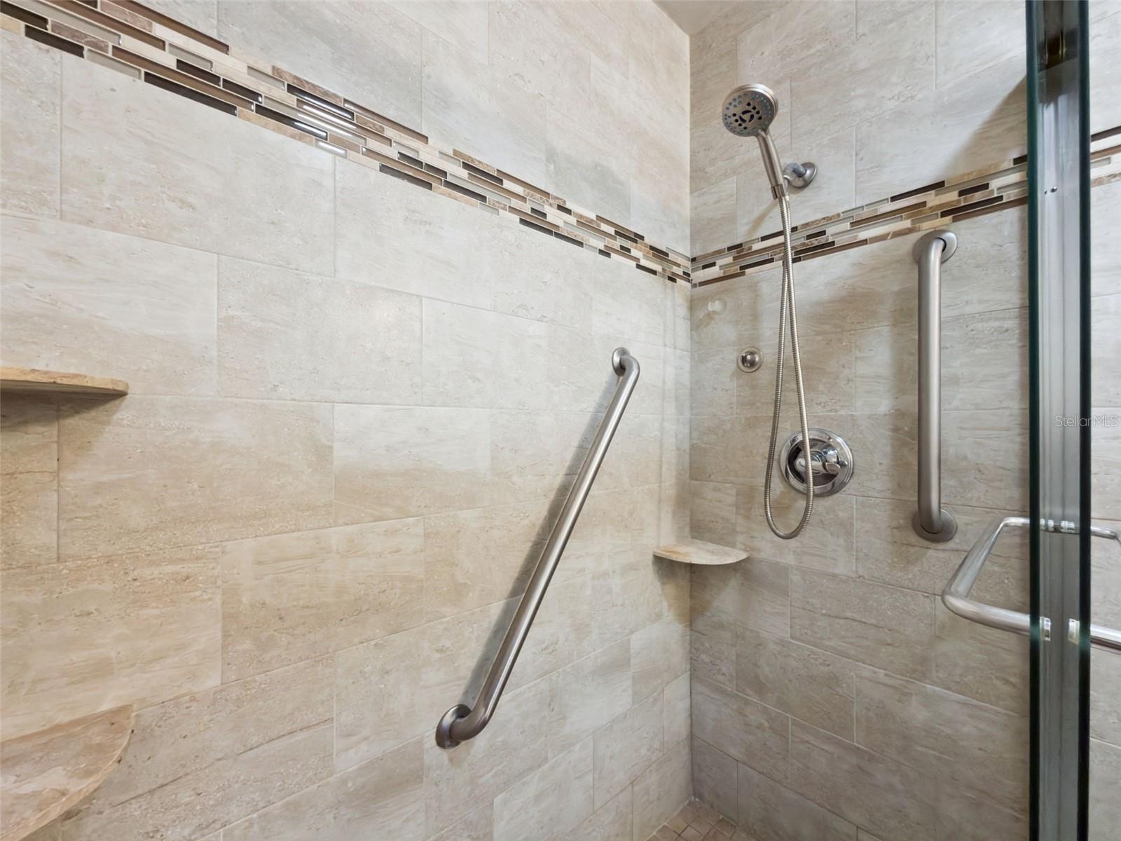 Stunning en suite, glass-enclosed shower with floor-to-ceiling and designer linear tiles plus built-in shelves.