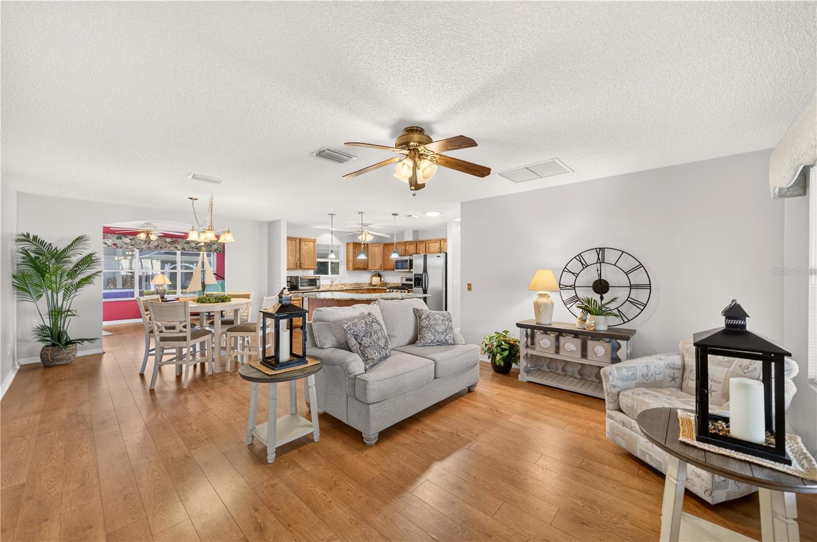 Bright and welcoming living room featuring attractive wood-look flooring, neutral wall colors, a ceiling fan, and an open layout connecting the dining area and kitchen. Bright and welcoming living room featuring attractive wood-look flooring, neutral wall colors, a ceiling fan, and an open layout connecting the dining area and kitchen.